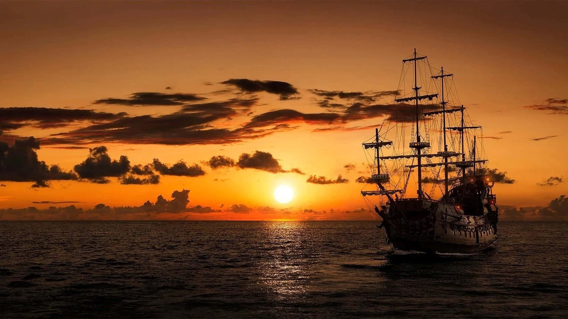 船 桌布 壁紙 — 一艘高大的帆船在平靜的海面上航行，夕陽在散落的雲層後方呈現出火熱的橙色和金色色調。
