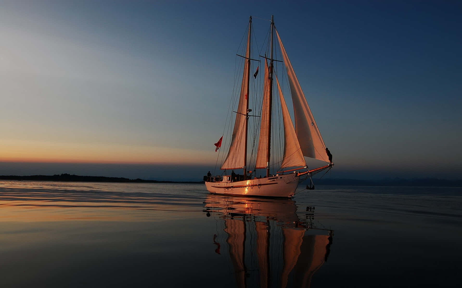 Sailboat 桌布 壁紙 — 一艘高大的船在日落時分平靜地航行，船帆在漸變色的天空下閃耀著橙色光芒，完美地倒映在平靜的水面上。