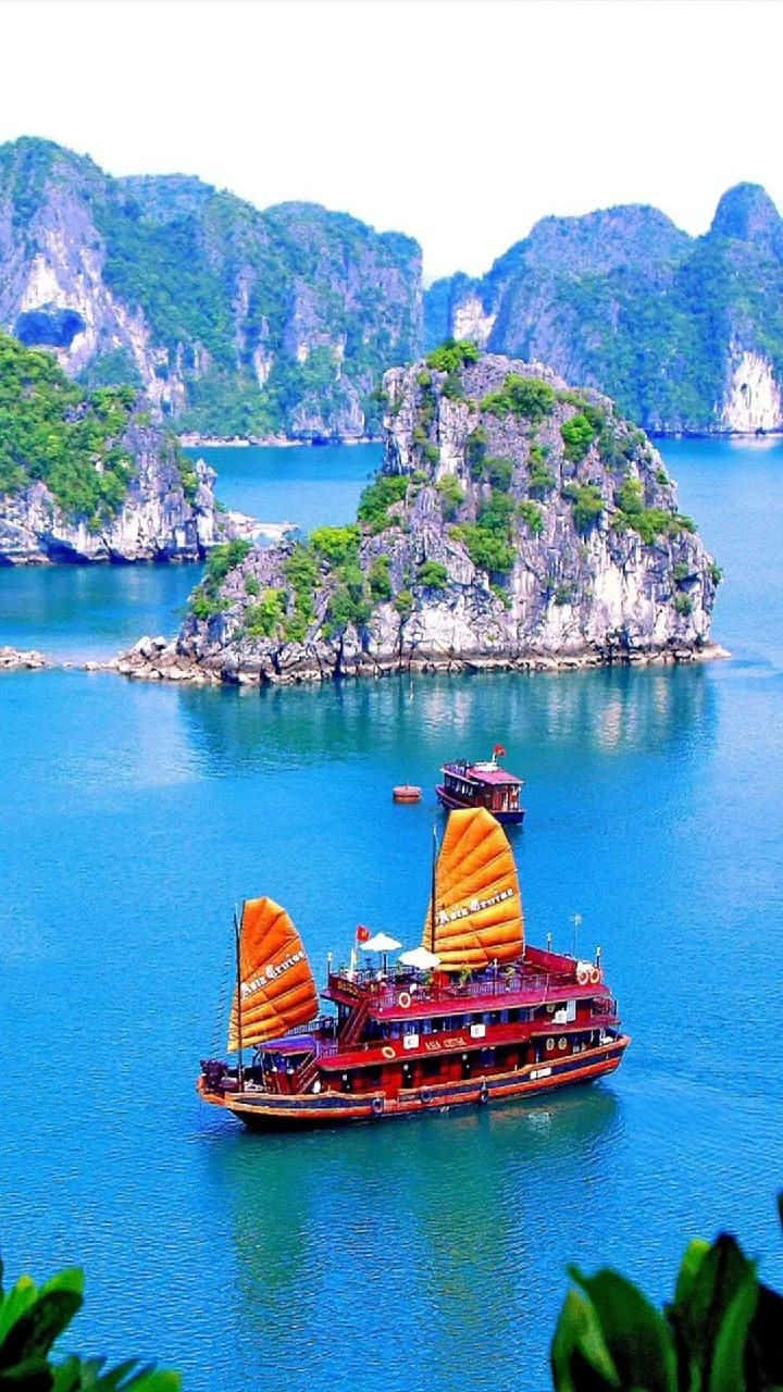Vietnam 桌布 壁紙 — 一艘鮮紅色的中式帆船帶著橙色帆，在碧綠的海水中滑行，四周是高聳的石灰岩喀斯特地貌，覆蓋著茂密的綠色植被。