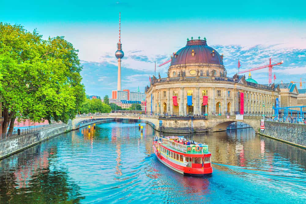 Berlin 桌布 壁紙 — 一艘鮮紅色的觀光船沿著閃閃發光的運河滑行，經過歷史悠久的圓頂建築和茂密的綠樹，在明亮的藍天下。