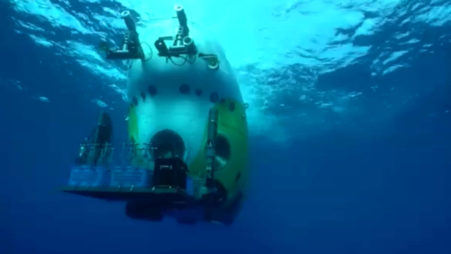 Mariana Trench 桌布 壁紙 — 一艘黃白相間的潛水器在深藍色的海水中滑行，陽光從上方穿透而下。