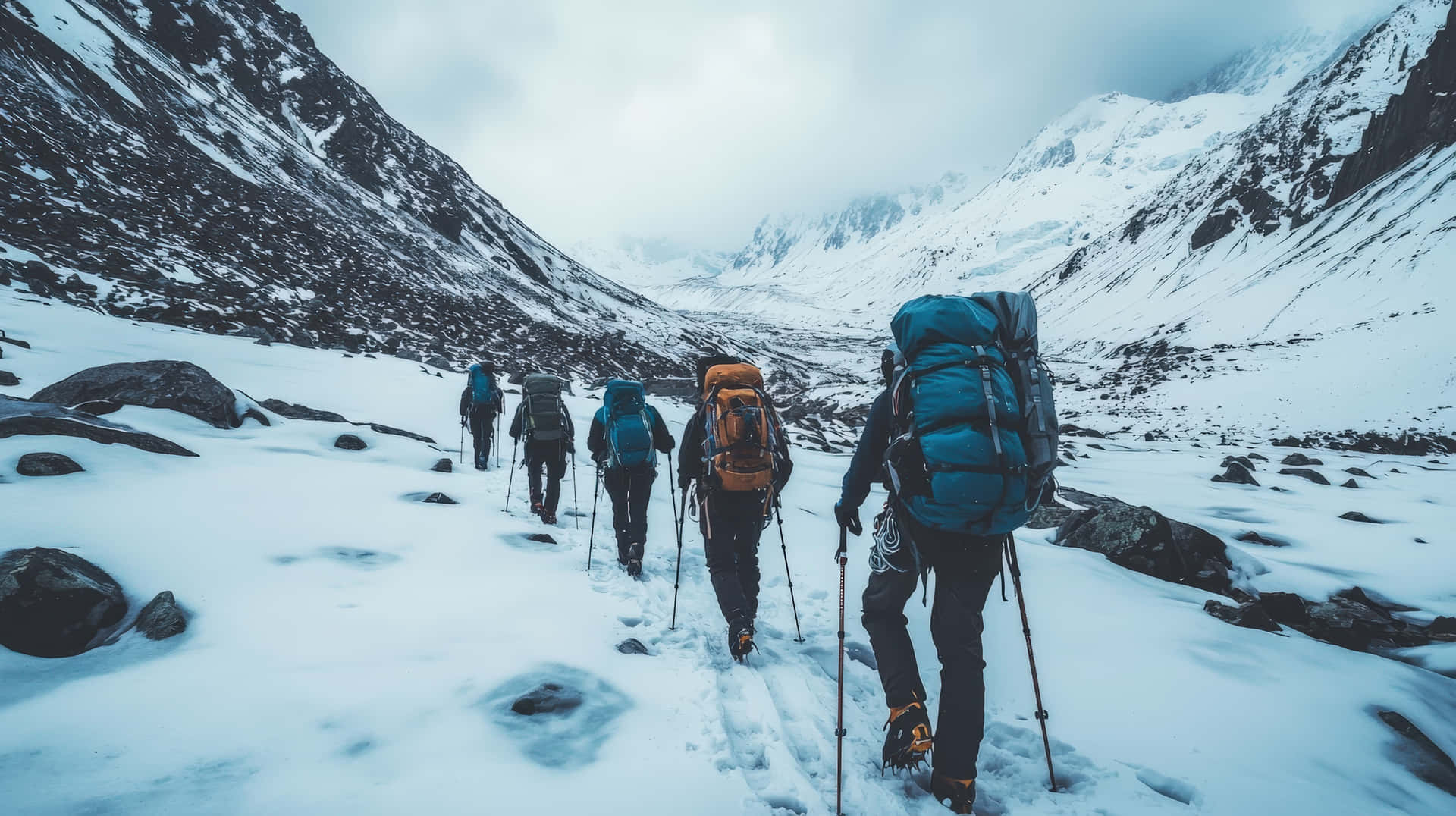 A team of hikers with backpacks and trekking poles journey through a rugged, snow-covered mountain 壁紙 — 一行背著大背包和登山杖的遠足者，在陰天之下穿越積雪的山谷。