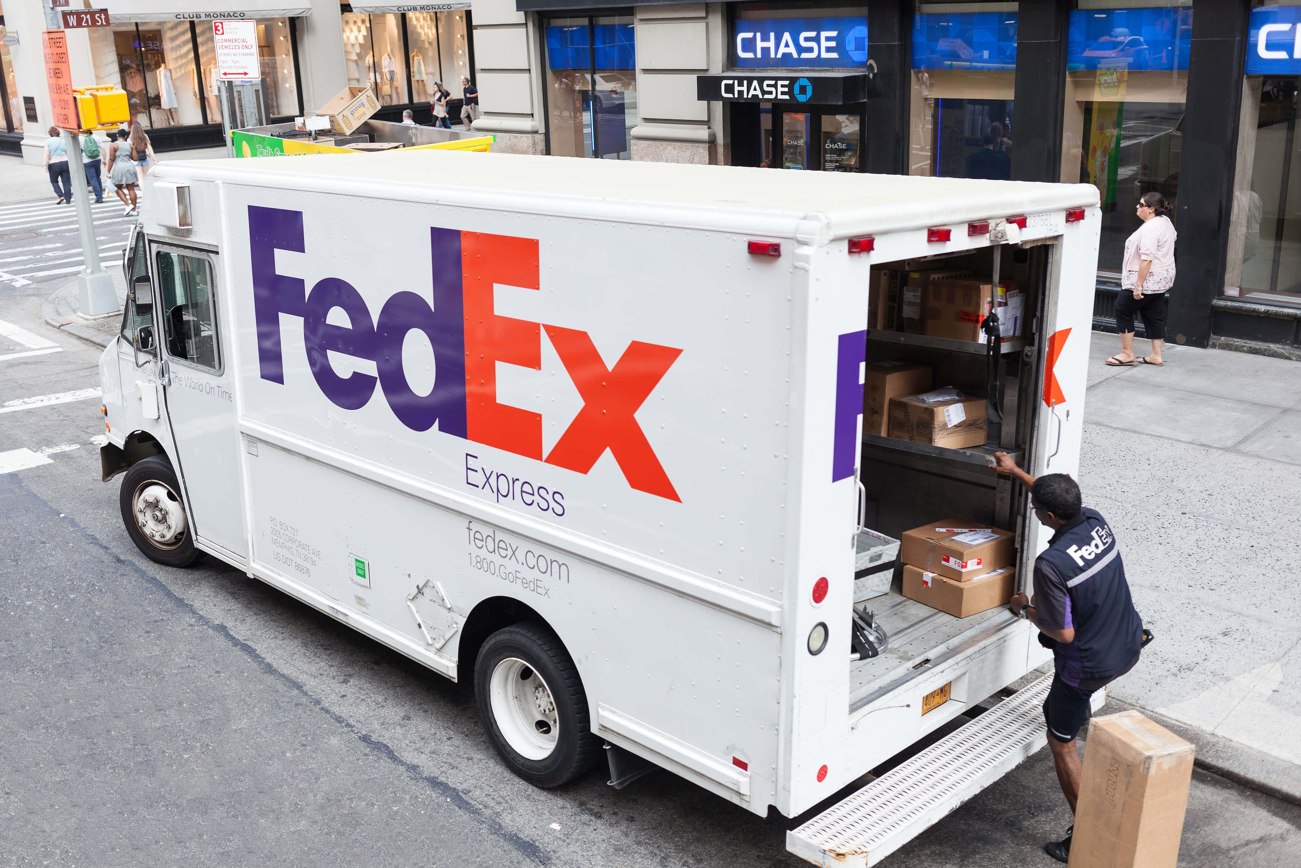 聯邦快遞 桌布 壁紙 — 一輛 FedEx Express 送貨車停在城市街道上，司機正在將包裹裝入打開的後門。