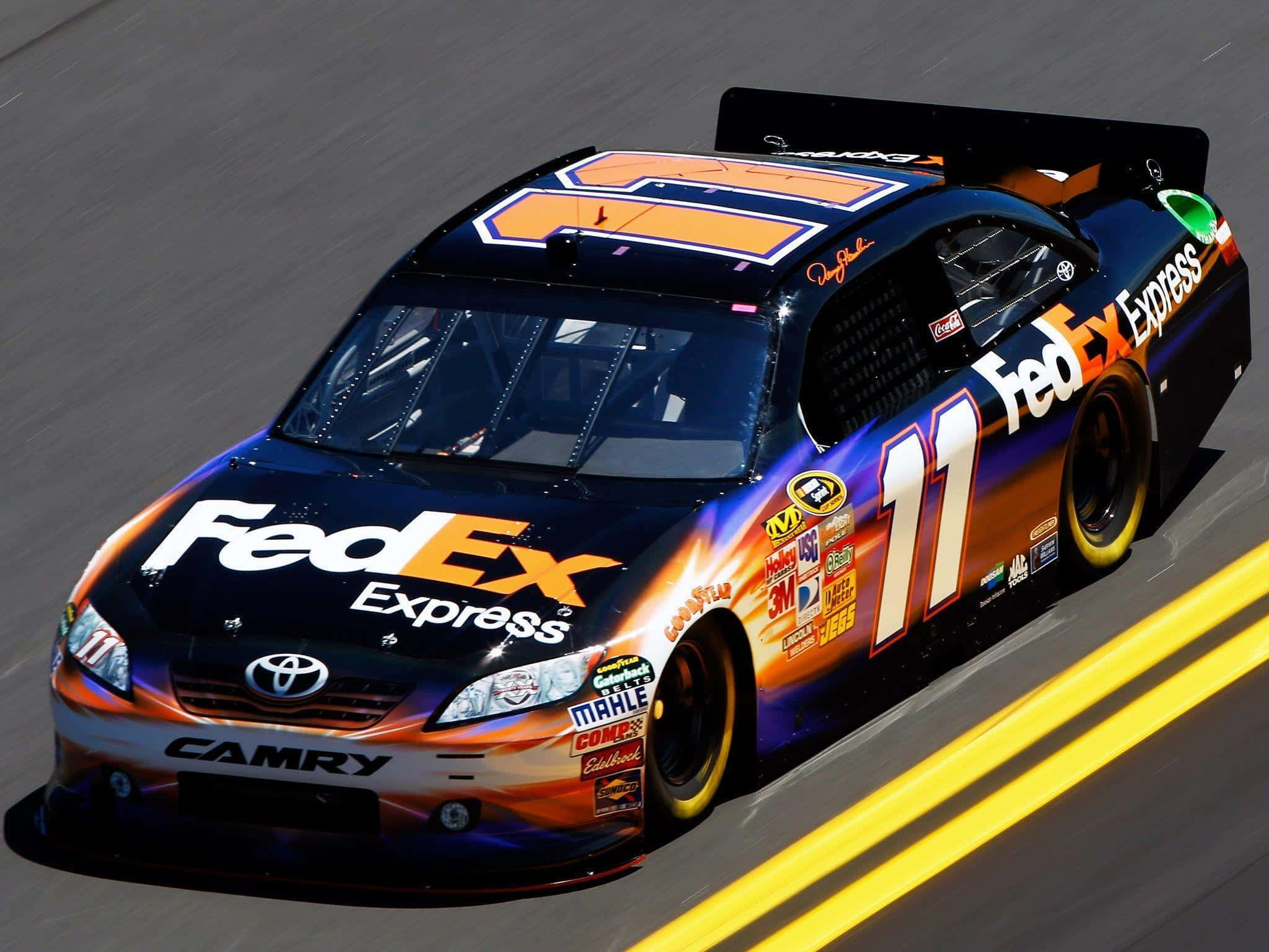 nascar 桌布 壁紙 — 一輛 FedEx Express Toyota Camry 賽車在賽道上疾馳，帶有動態模糊和明亮的黃色車道標記。