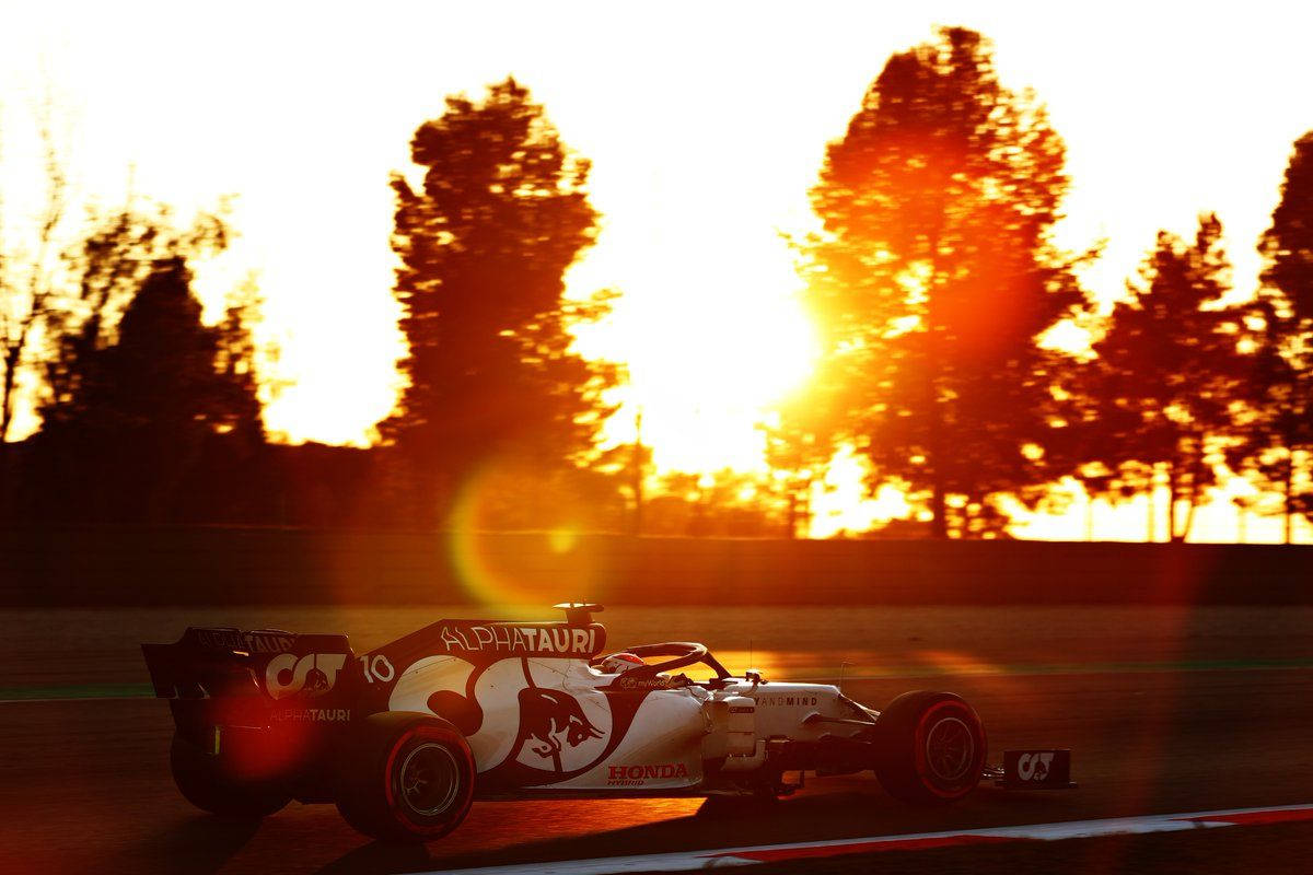 Sun Rays 桌布 壁紙 — 一輛 Formula 1 AlphaTauri 賽車在日落時分奔馳，背後有剪影樹木襯托著熾熱的橙色光芒。