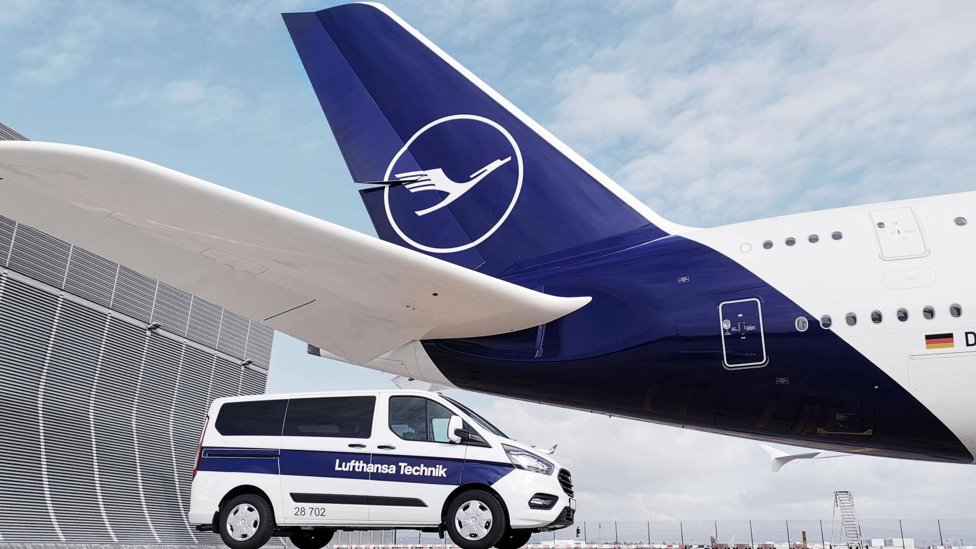 飛機 桌布 壁紙 — 一輛 Lufthansa Technik 服務貨車停放在機場機庫中 Lufthansa 飛機的尾部下方。