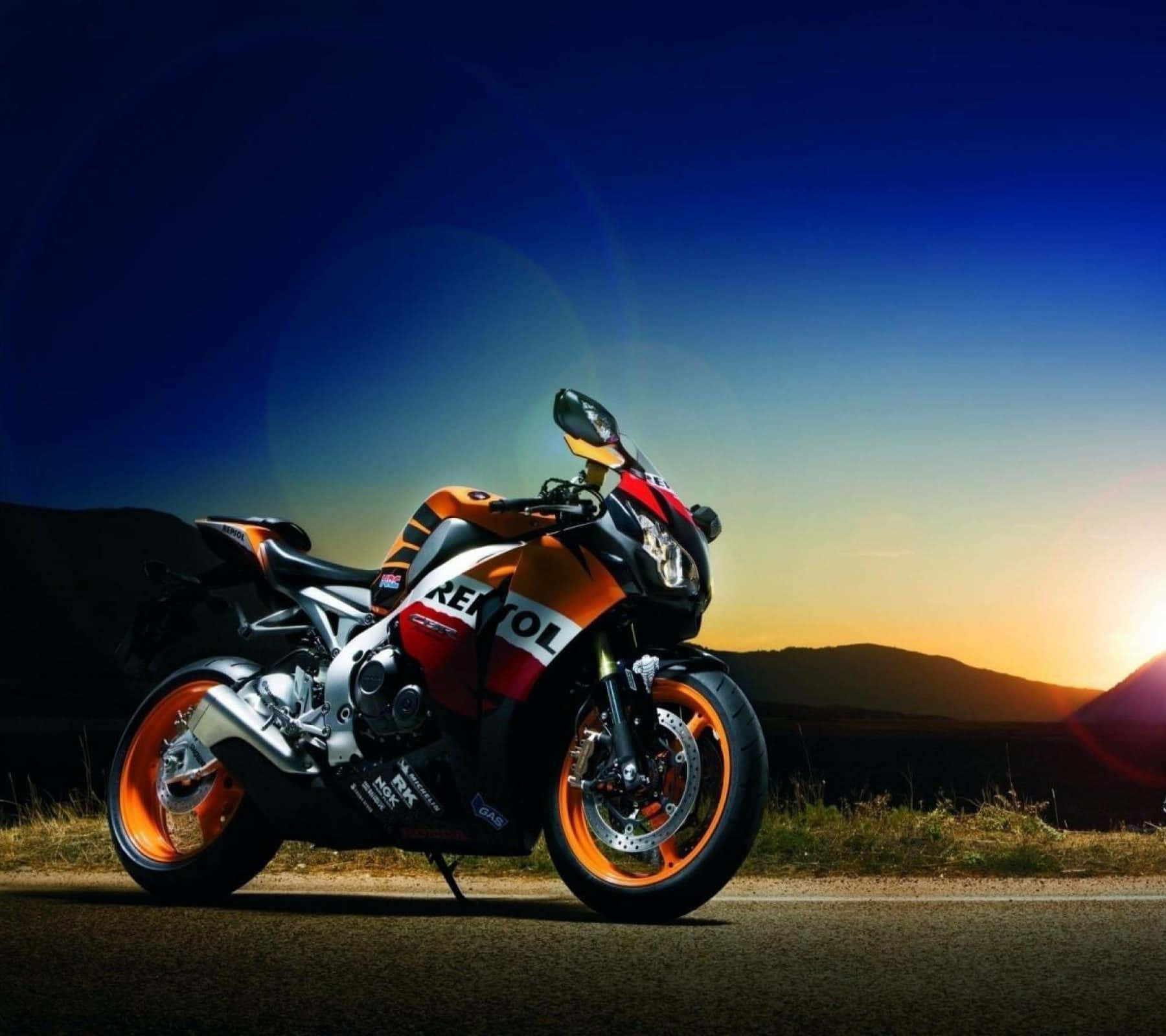 機車 桌布 壁紙 — 一輛 Repsol 賽車摩托車在充滿活力的日落天空下閃閃發光，配備橙色車輪和醒目的品牌標誌。