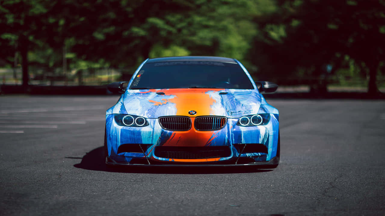 720p Bmw 桌布 壁紙 — 一輛BMW跑車帶有鮮明的藍色和橙色塗鴉風格塗裝，停在樹下的柏油路面上。