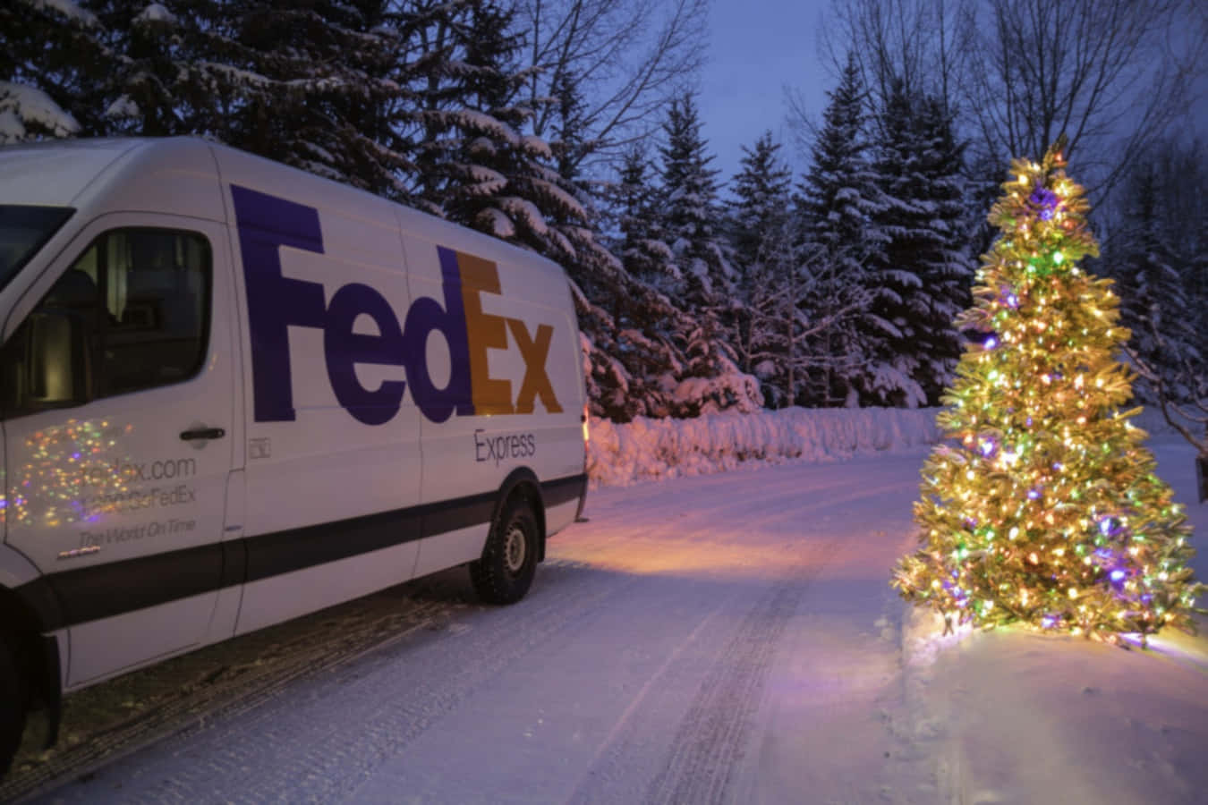 聯邦快遞 桌布 壁紙 — 一輛FedEx貨車停泊在黃昏時分白雪覆蓋的冬季森林中一棵明亮照明的聖誕樹旁。