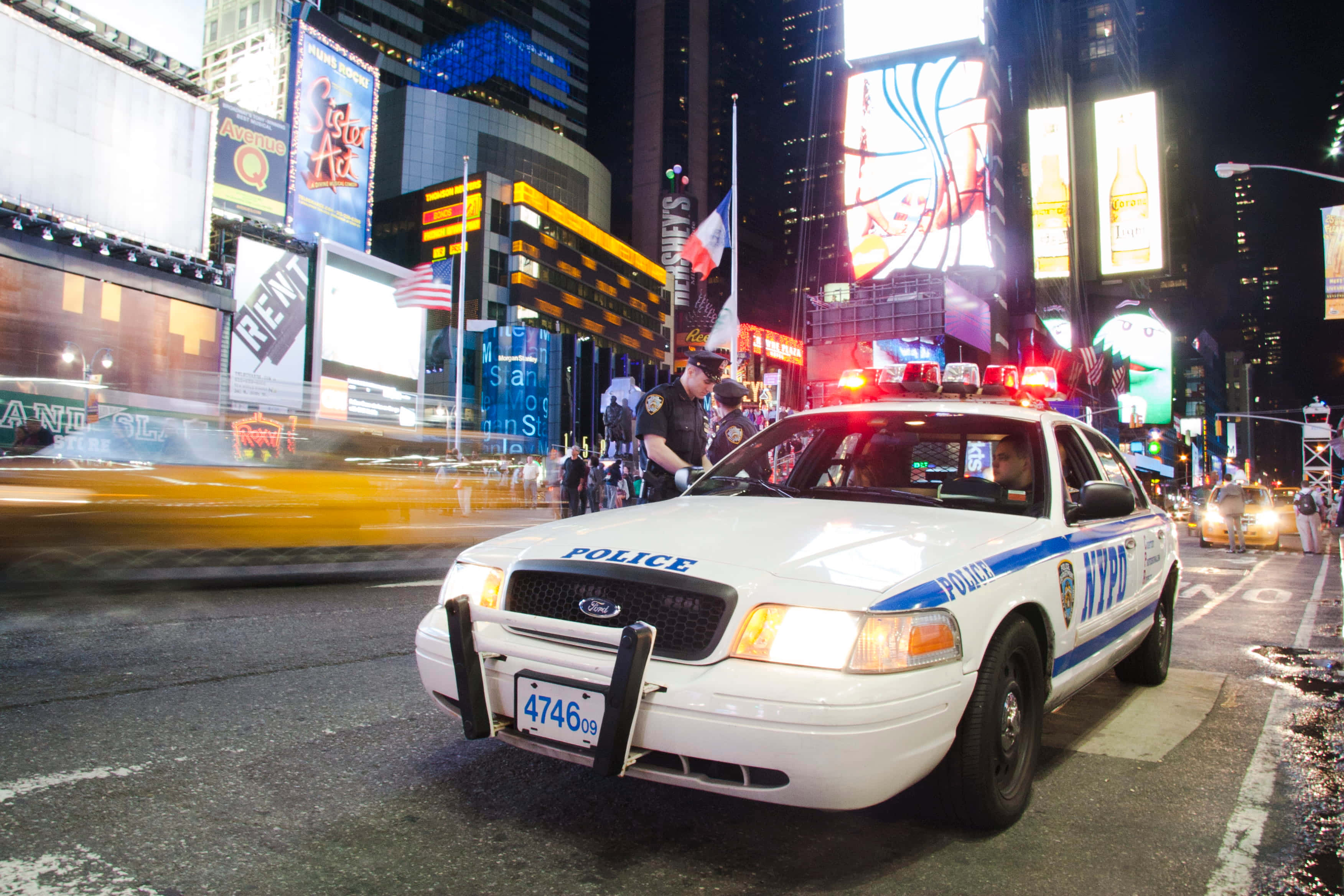 Ford Crown Victoria 桌布 壁紙 — 一輛NYPD警車在夜晚閃爍著警燈，停在時代廣場繁忙的霓虹燈街道上。