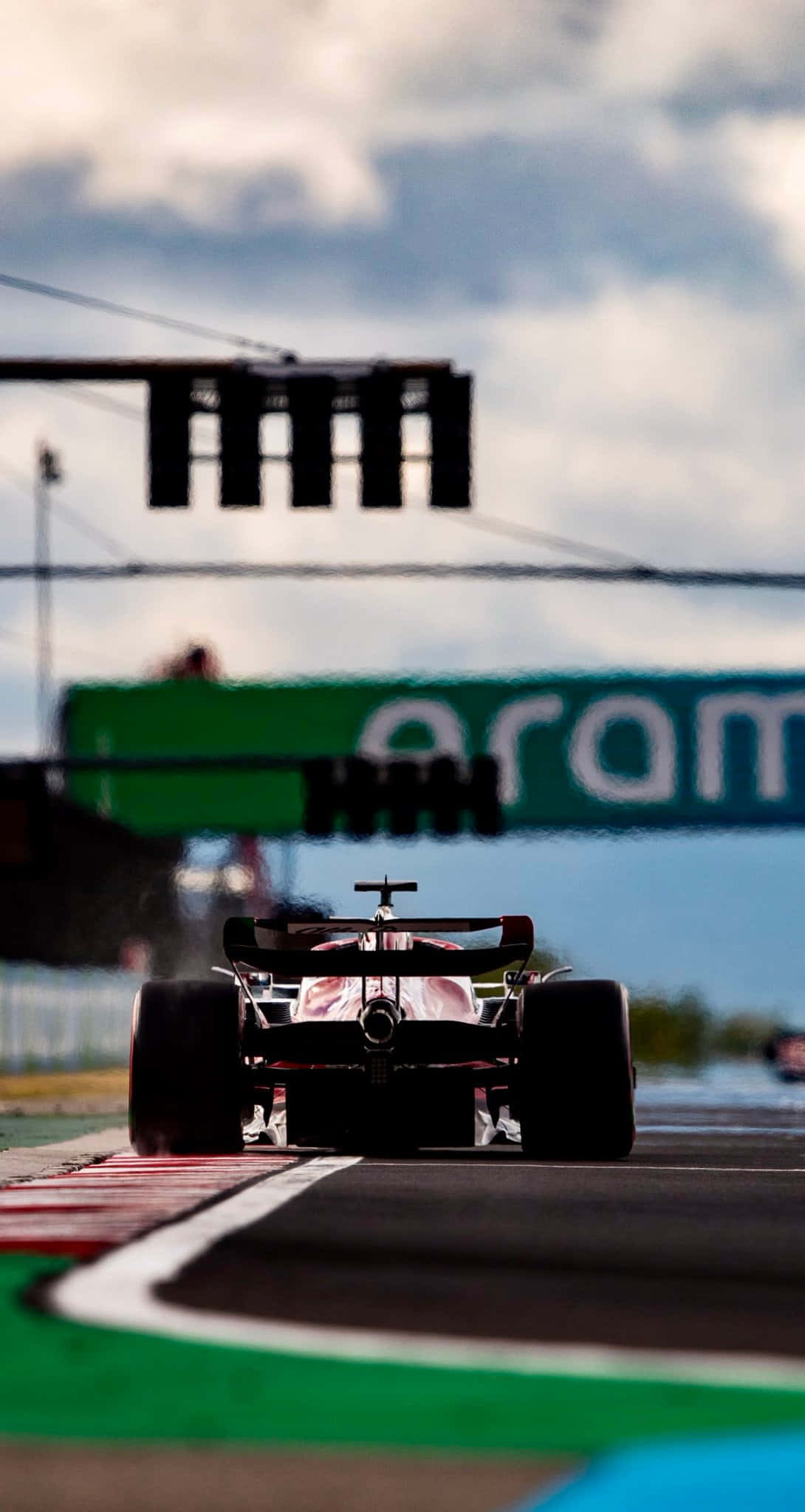 Formula 1 iPhone 桌布 壁紙 — 一輛一級方程式賽車在陰天下的賽道上奔馳，賽道有紅色和白色的路緣石。