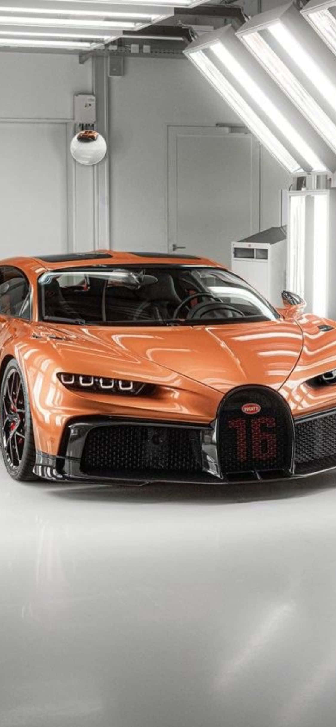 iPhone Xs Bugatti 桌布 壁紙 — 一輛亮橙色Bugatti超跑，前格柵上帶有發光的「16」，停在簡約白色車庫中，上方是明亮的螢光燈。