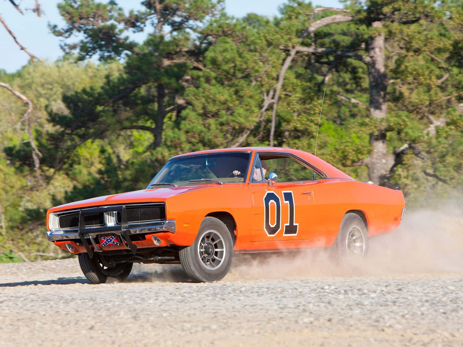 General Lee 車 桌布 壁紙 — 一輛亮橙色的1970年道奇Charger，側面有「01」字樣，在碎石路上疾馳，揚起灰塵，背景是松樹。