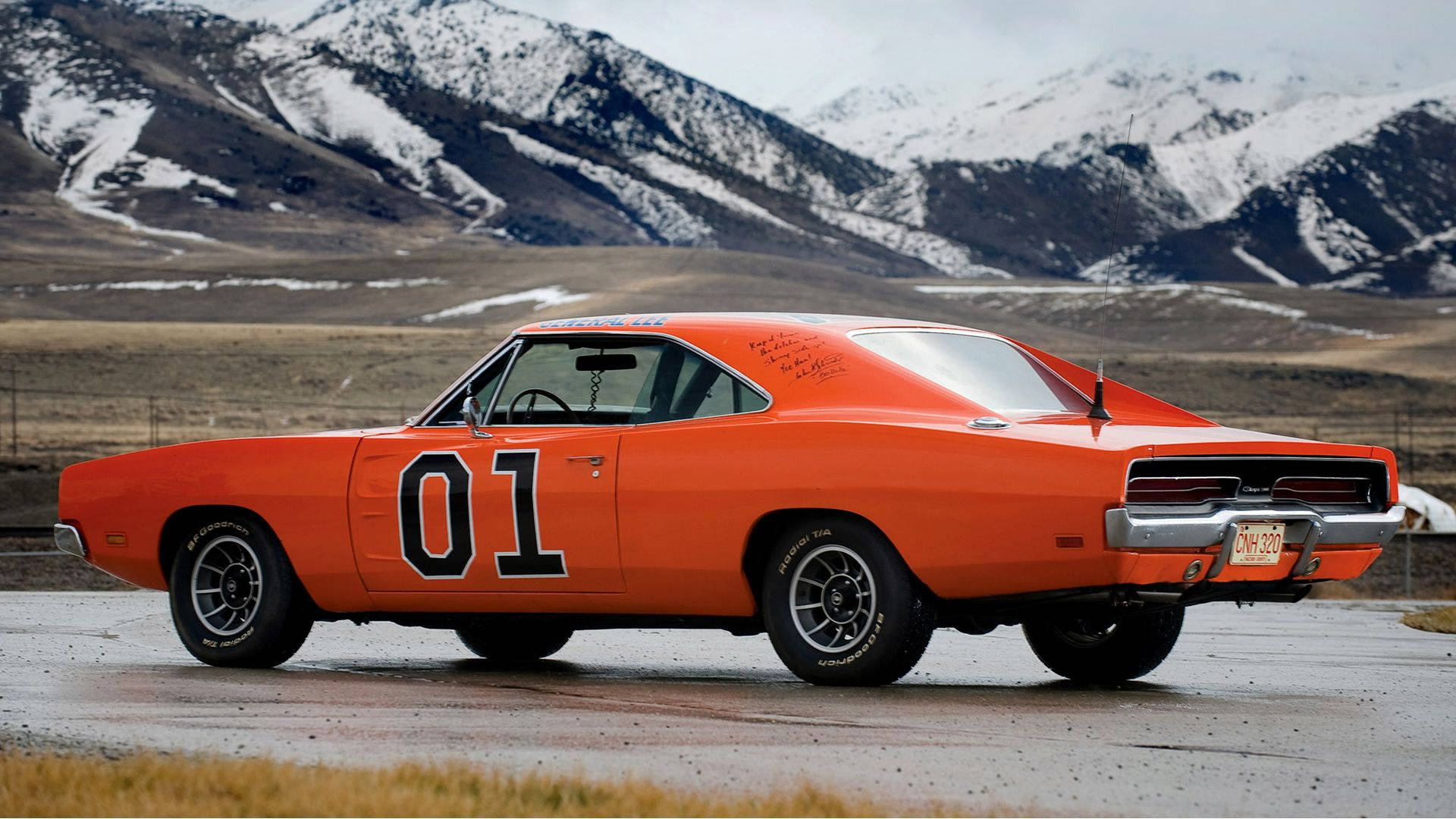 cars 桌布 壁紙 — 一輛亮橙色的1970年道奇Charger，帶有黑色01號碼，停泊在濕滑的道路上，背景是積雪的山脈。