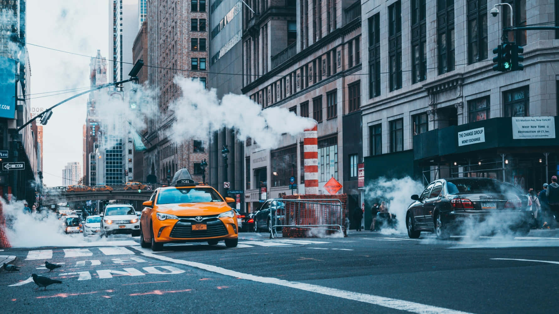 taxi 桌布 壁紙 — 一輛亮橙色的計程車在煙霧瀰漫的市區街道上行駛，人孔蓋冒出蒸氣，汽車在高聳建築物之間停滯不前。