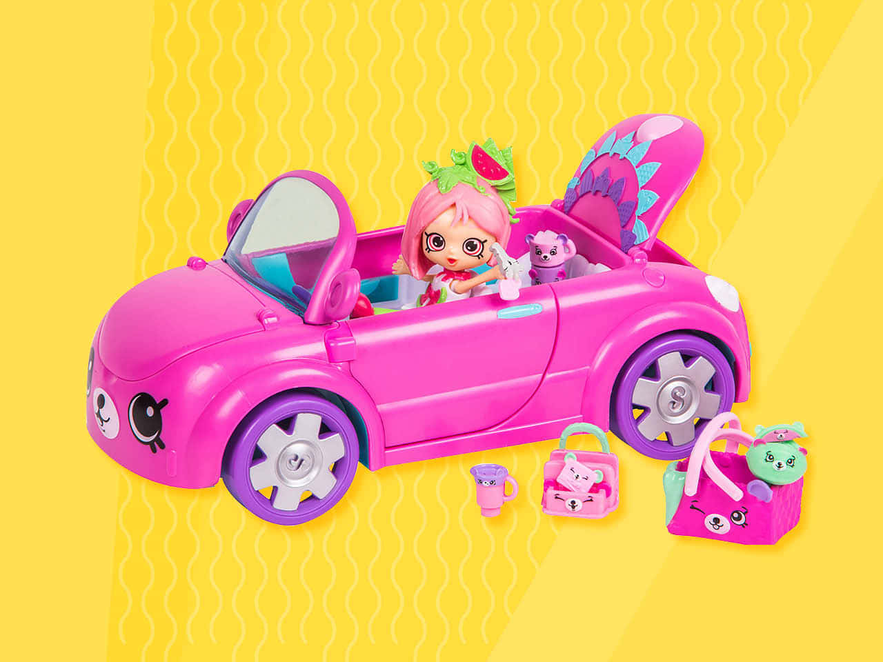 Shopkins 桌布 壁紙 — 一輛亮粉紅色玩具敞篷車，裡面有娃娃和毛絨寵物，放在黃色波浪背景上，附有配件。