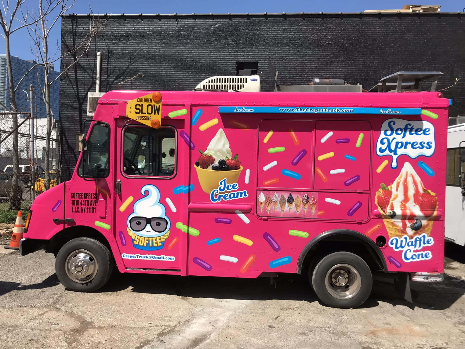 Ice Cream Truck 桌布 壁紙 — 一輛亮粉色的冰淇淋車，上面覆蓋著五顏六色的糖粒和卡通圖案，停在陽光明媚的城市街道上。