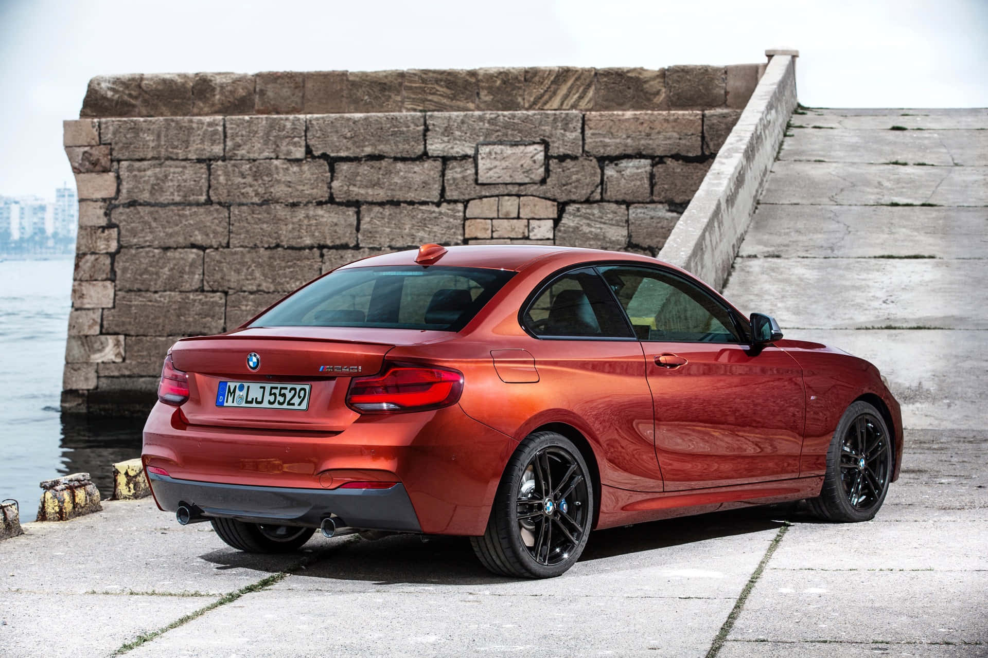 Bmw 2 Series 桌布 壁紙 — 一輛亮紅色BMW 2系列轎跑車停泊在風化石碼頭上，旁邊是平靜的水面，天空多雲。