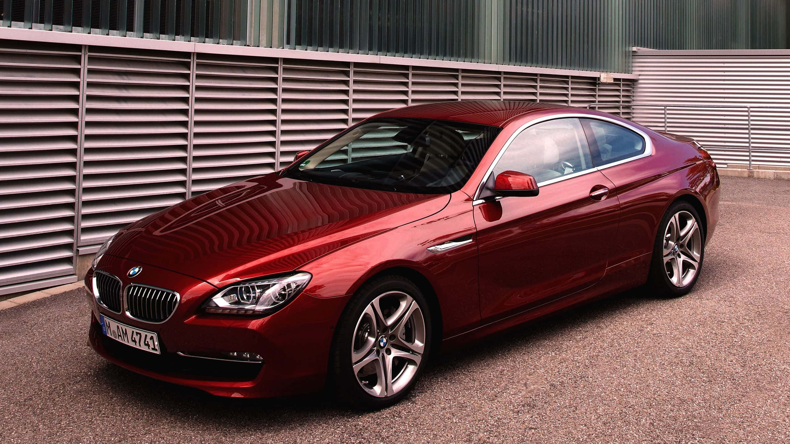 Bmw 6 Series 桌布 壁紙 — 一輛亮紅色BMW 6系列雙門轎跑車停在碎石上，旁邊是金屬條紋牆，在明亮的日光下。