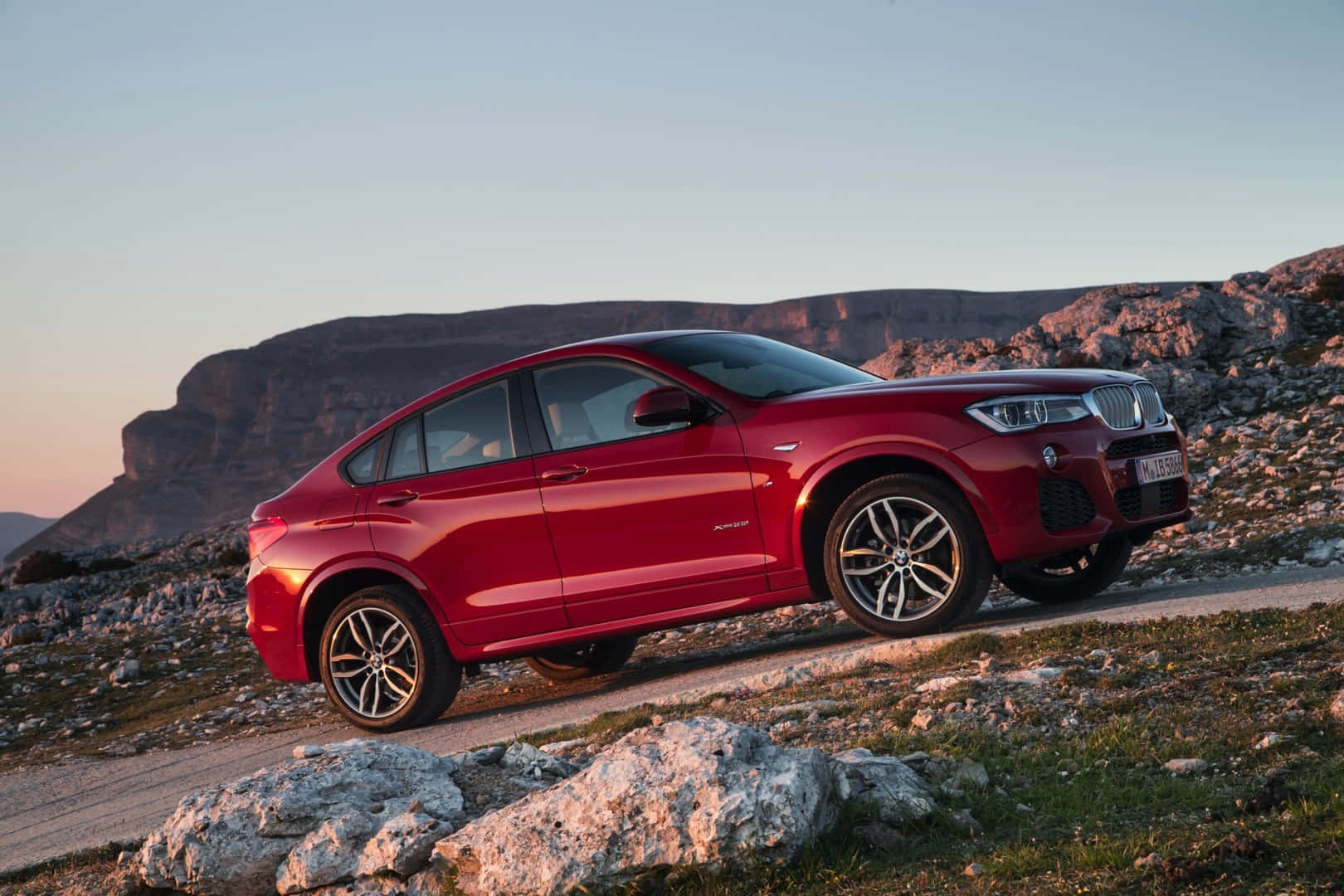 Bmw X4 桌布 壁紙 — 一輛亮紅色BMW X4 SUV停泊在日落時分的岩石山路上，背景是崎嶇的懸崖。