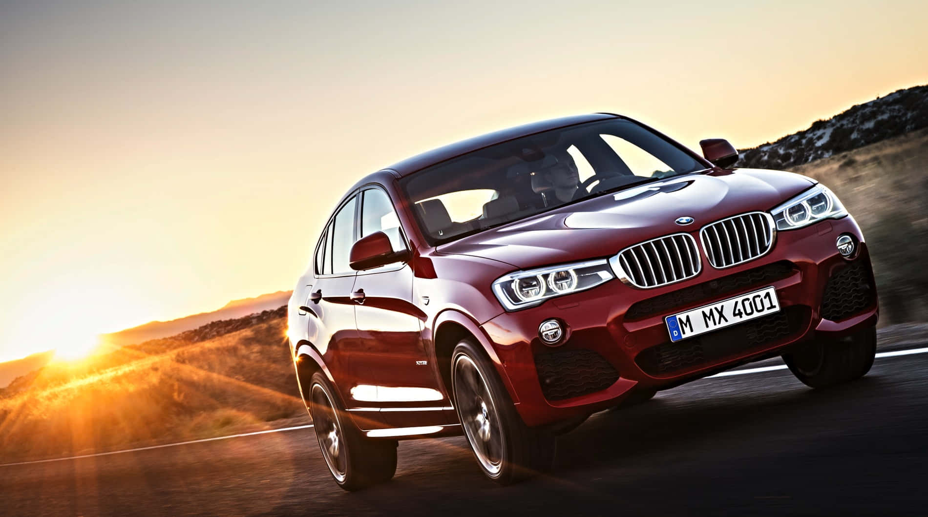Bmw X4 桌布 壁紙 — 一輛亮紅色BMW X4 SUV在日落時分沿沙漠公路疾駛，背後太陽散發出金色光芒。