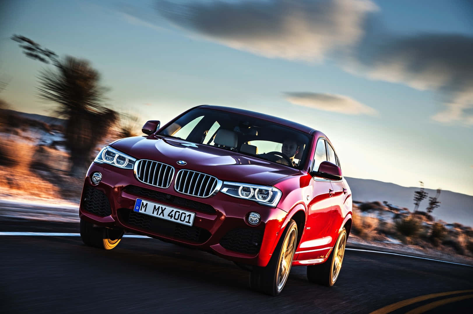 Bmw X4 桌布 壁紙 — 一輛亮紅色BMW X4在日落時分沿沙漠公路疾馳，帶有模糊動態和金色輪圈。