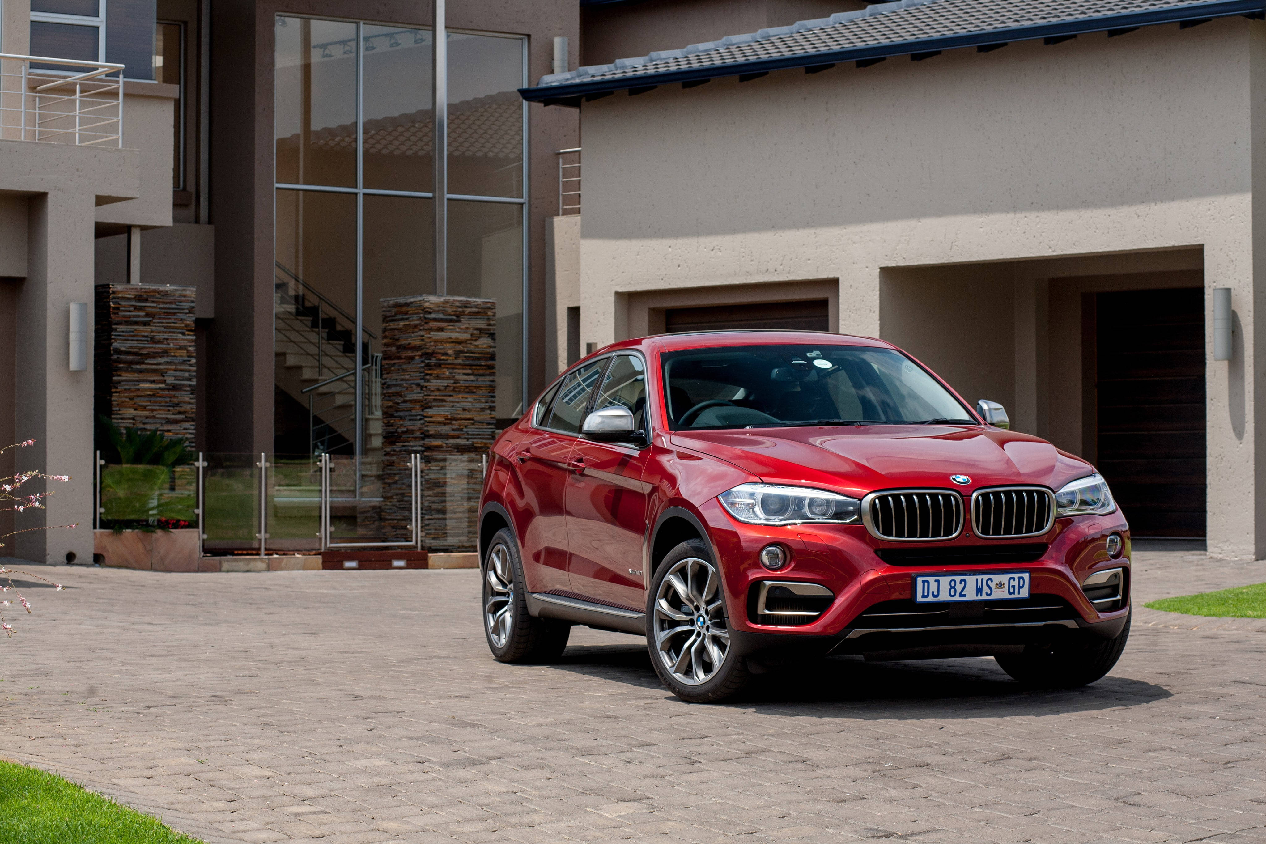 m 桌布 壁紙 — 一輛亮紅色BMW X6 SUV停放在現代化房屋前的石頭車道上，房屋有玻璃牆和石柱。