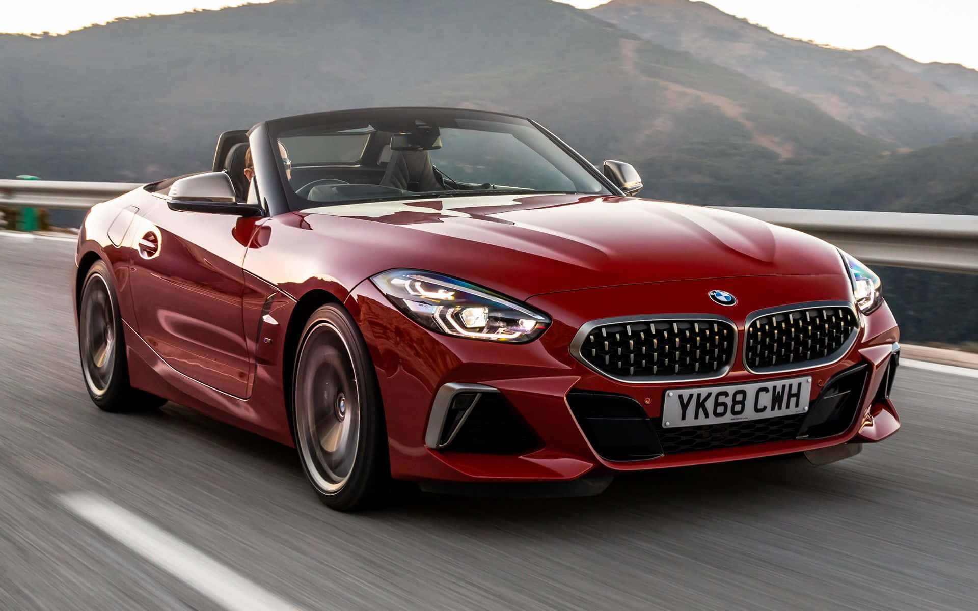 Bmw Z4 桌布 壁紙 — 一輛亮紅色BMW Z4敞篷跑車在高速公路上飛馳，背景是模糊的動態和陽光照耀的山丘。