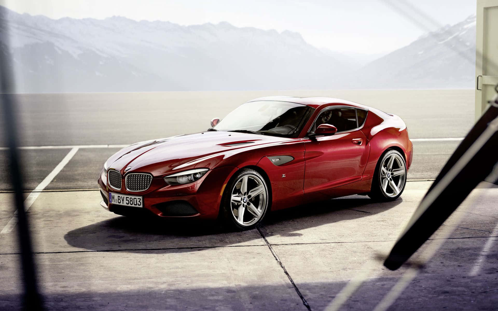 Bmw Z4 桌布 壁紙 — 一輛亮紅色BMW Z4跑車停放在混凝土場地上，背景有朦朧的雪山。