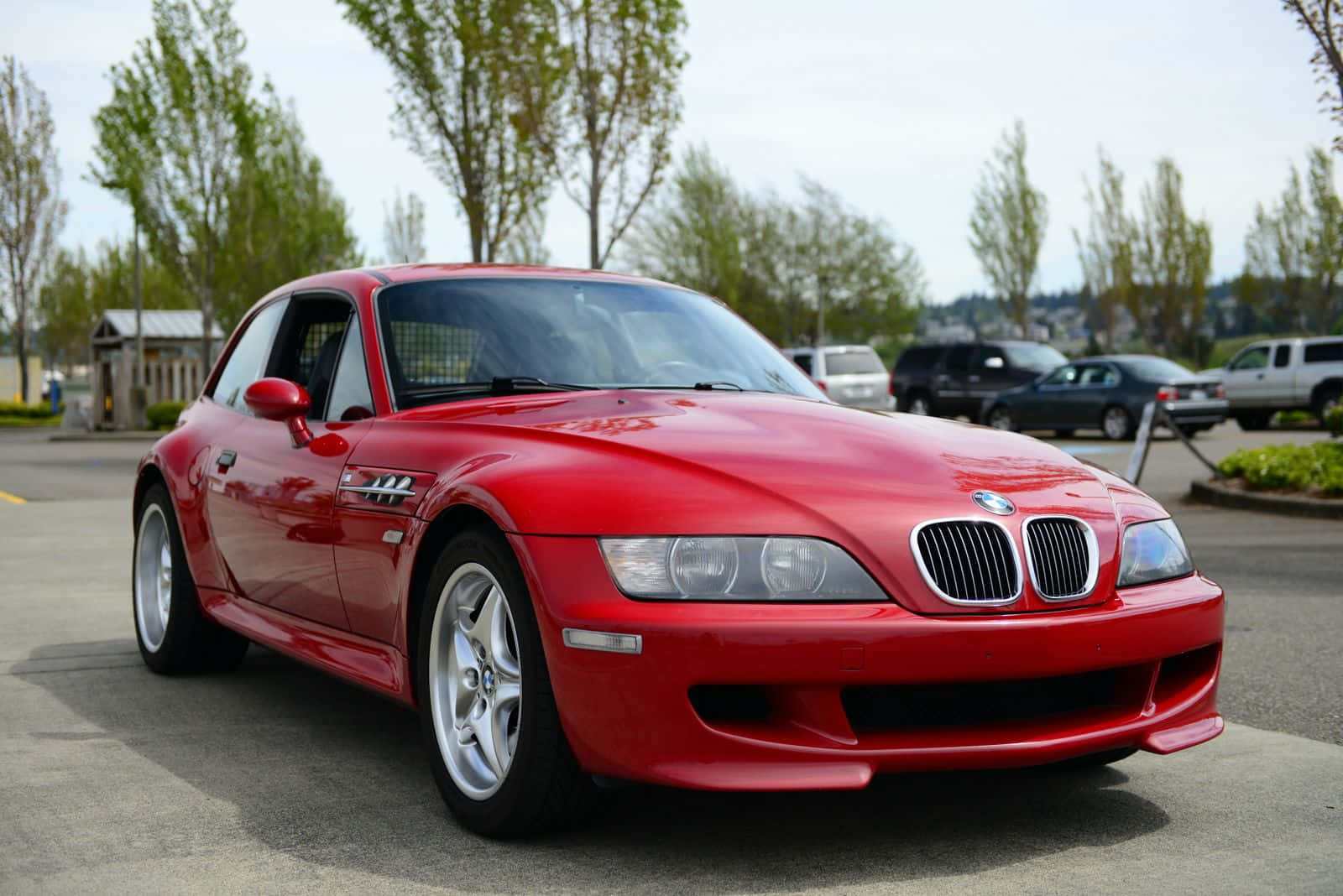 Bmw Z3 桌布 壁紙 — 一輛亮紅色BMW Z8跑車停放在柏油路上，背景有樹木和其他車輛。