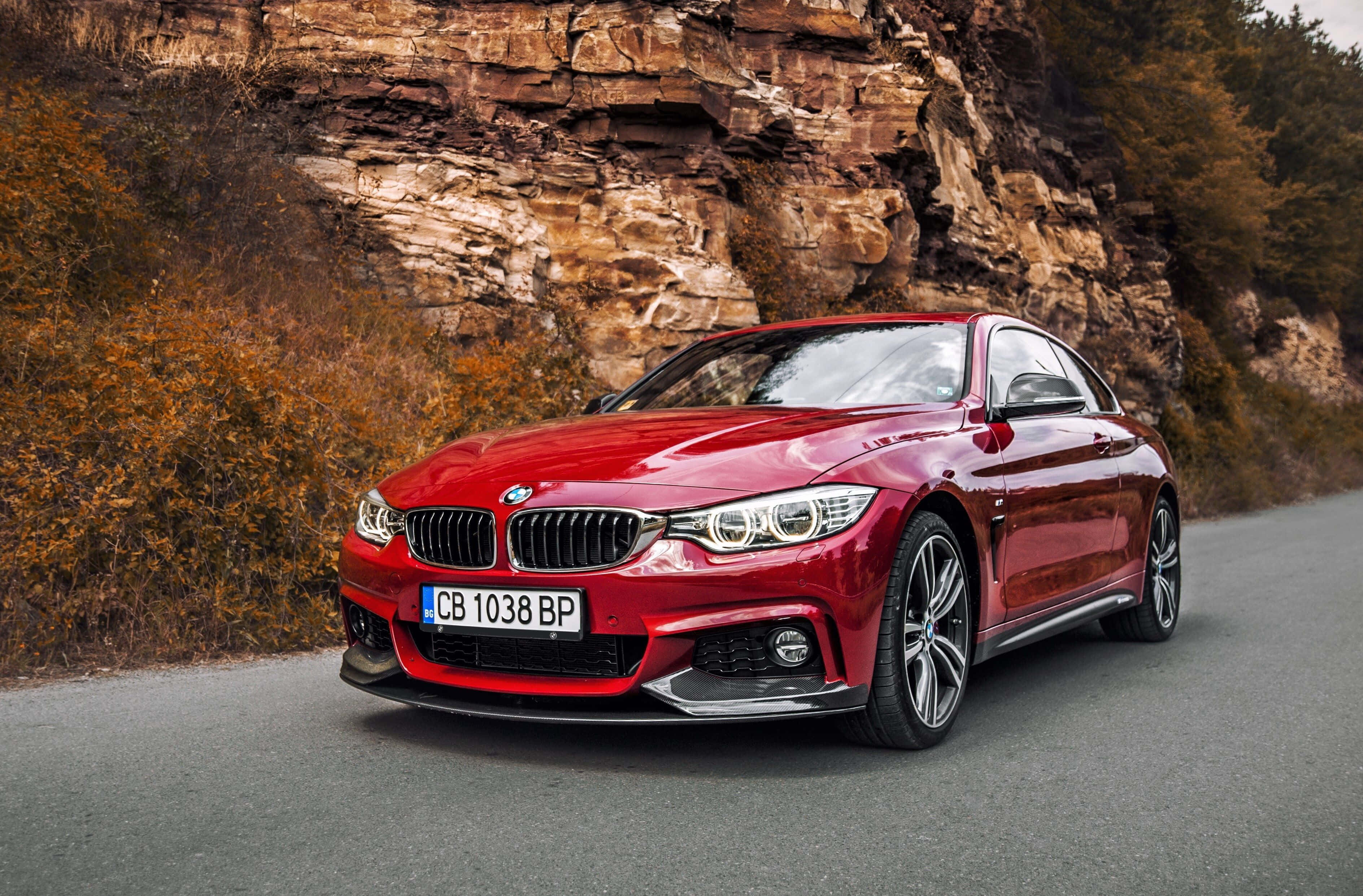 Bmw 440i 桌布 壁紙 — 一輛亮紅色BMW雙門跑車沿著蜿蜒的道路行駛，旁邊是佈滿秋葉的崎嶇懸崖。