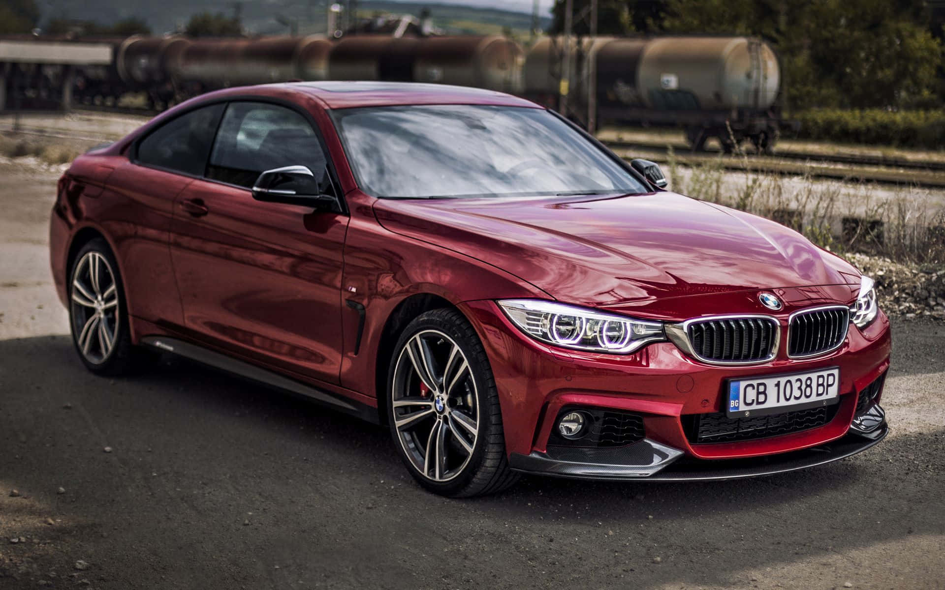 Bmw 4 Series 桌布 壁紙 — 一輛亮紅色BMW雙門轎跑車停泊在火車軌道附近，背景有工業儲罐。