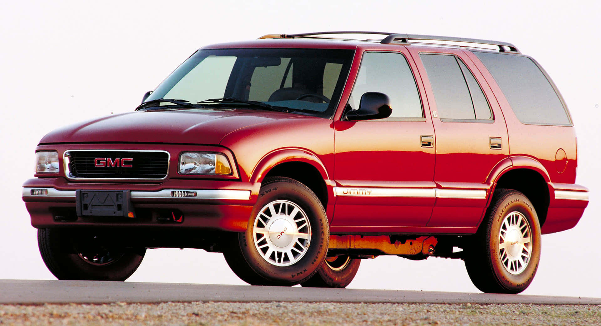 Gmc Jimmy 桌布 壁紙 — 一輛亮紅色GMC Yukon SUV停在礫石上，明亮的白色背景展示其鍍鉻飾件和合金輪圈。
