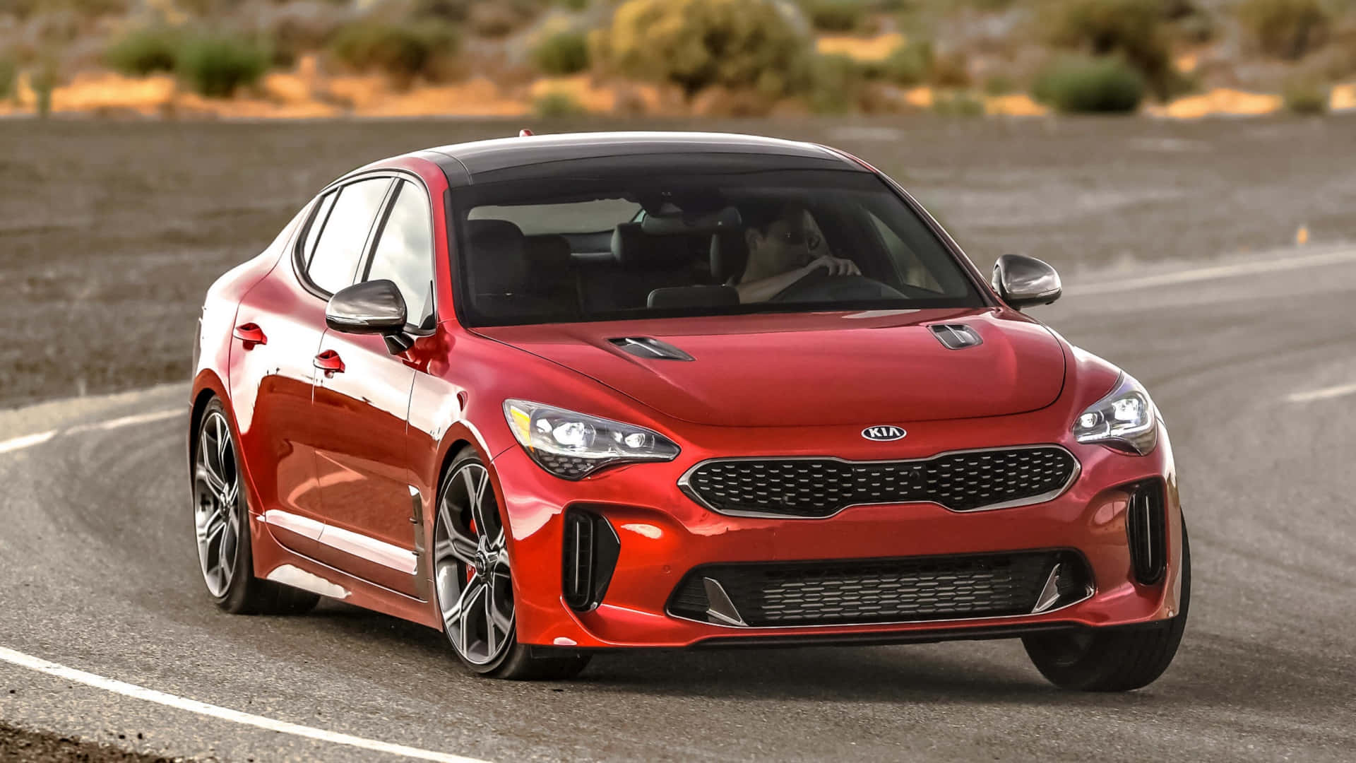 Kia Stinger 桌布 壁紙 — 一輛亮紅色Kia Stinger跑車在沙漠公路上飛馳，背景是崎嶇的地形。