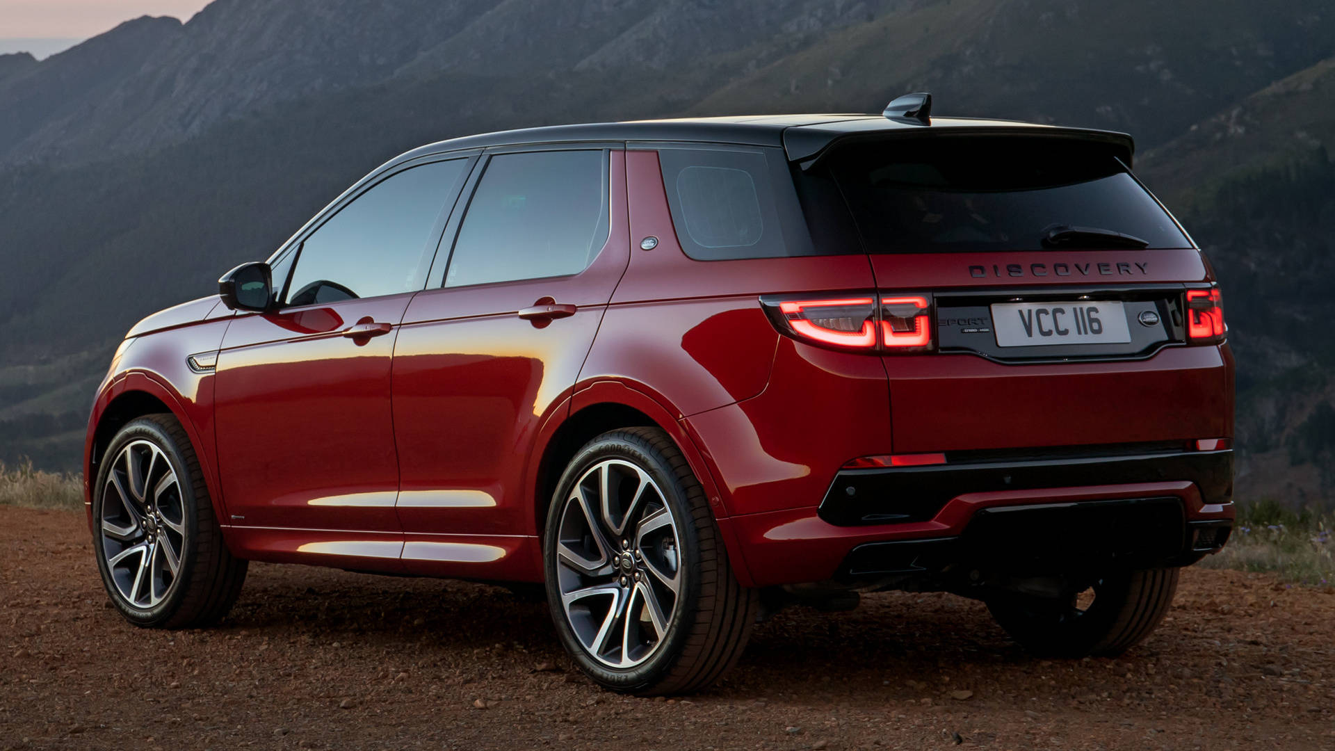 land rover iPhone 桌布 壁紙 — 一輛亮紅色Land Rover Discovery SUV停泊在泥土小徑上，背景是黃昏時崎嶇的山脈。