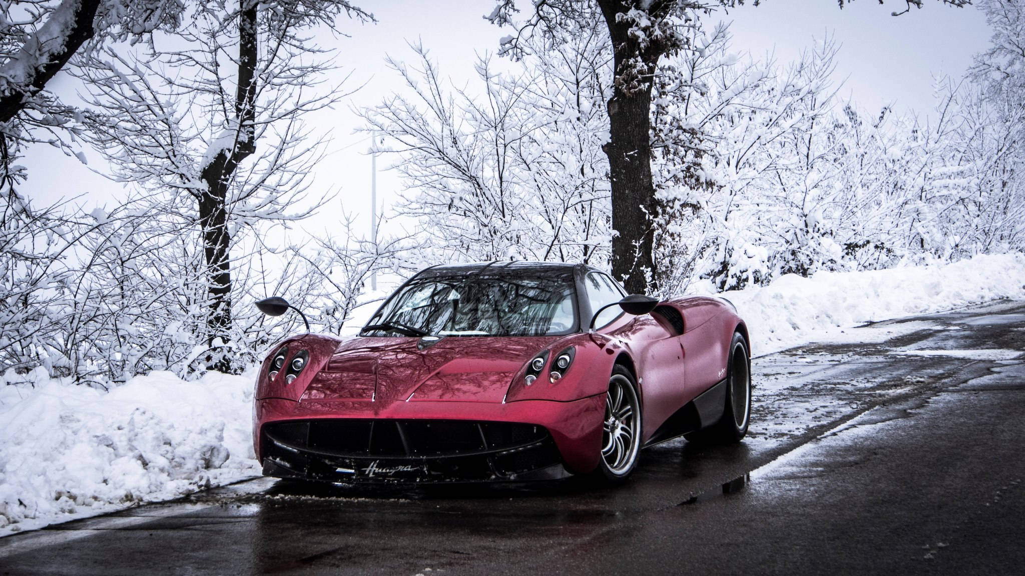 Pagani 桌布 壁紙 — 一輛亮紅色Pagani跑車停泊在積雪的路邊，周圍是光禿禿的樹木，潮濕的路面反射著陰沉的天空。