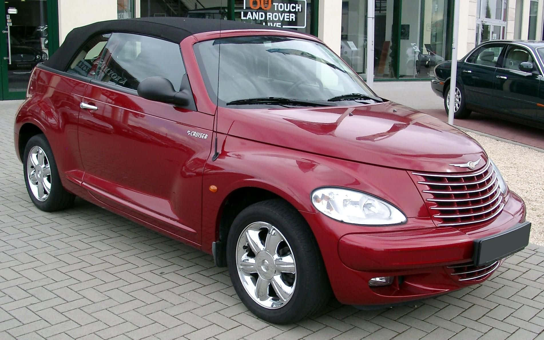 Chrysler Pt Cruiser 桌布 壁紙 — 一輛亮紅色PT Cruiser敞篷車停放在鋪砌的停車場上，背景有Land Rover經銷商。