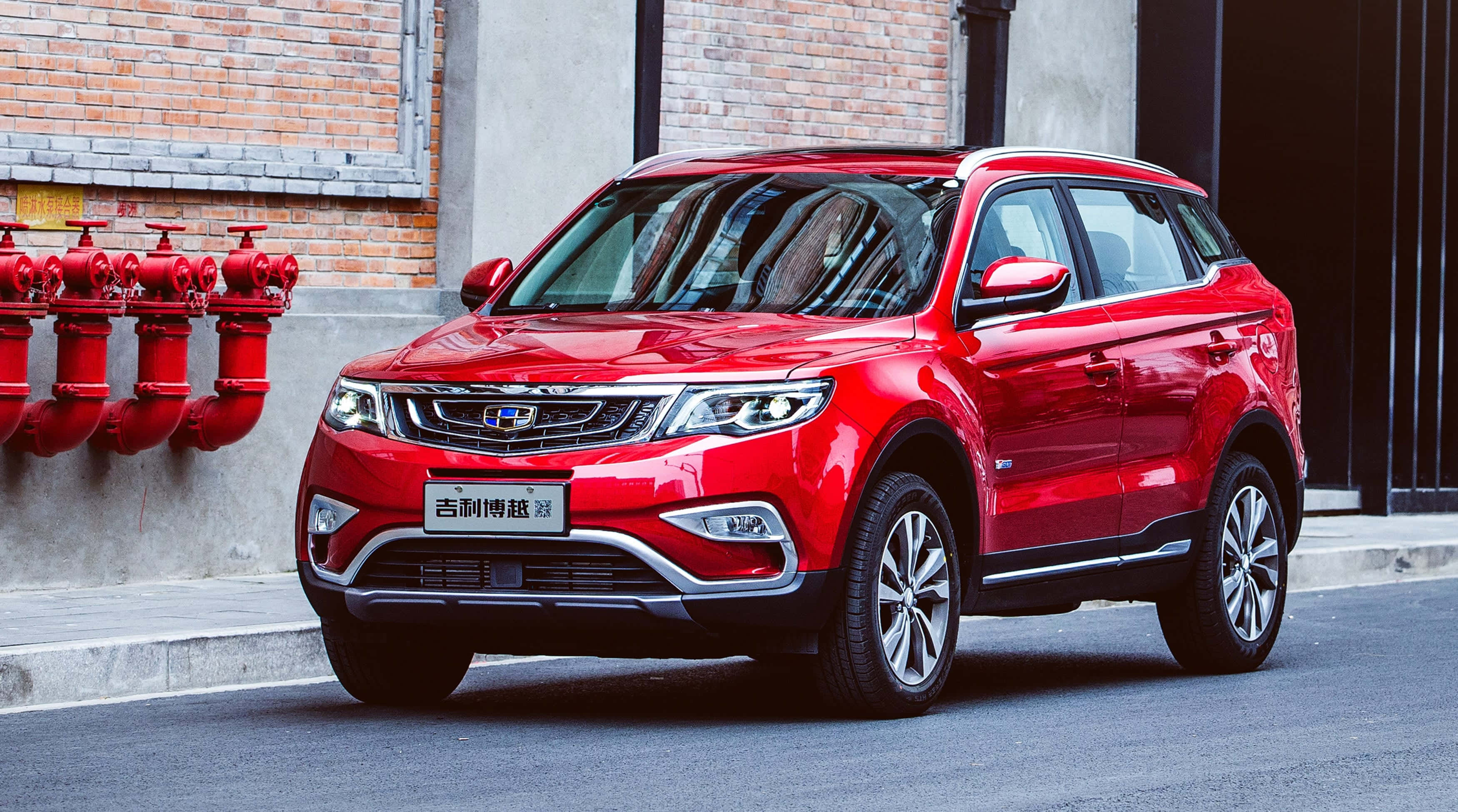 Geely 桌布 壁紙 — 一輛亮紅色SUV停放在城市街道上，旁邊是磚牆和紅色消防栓。