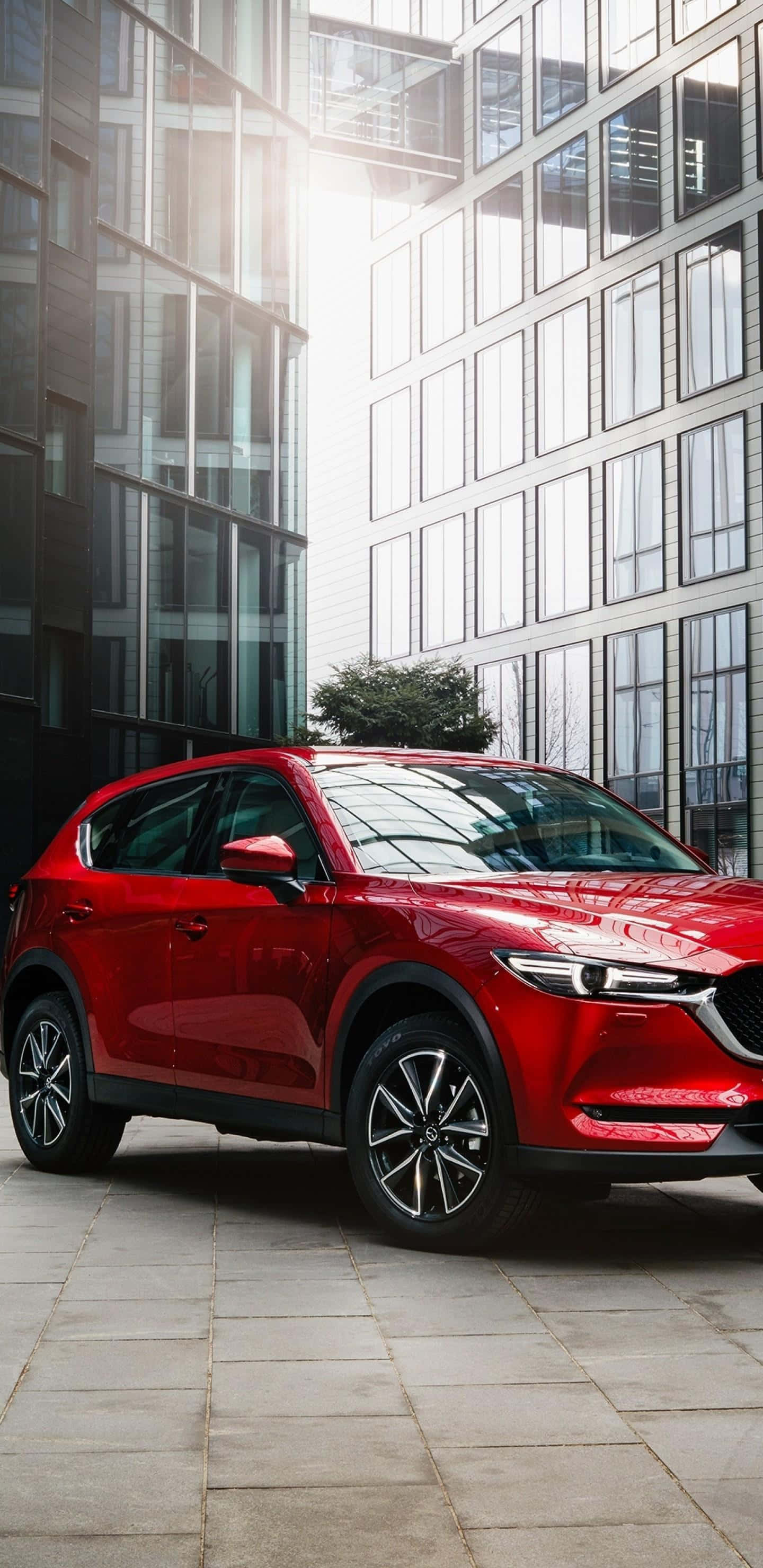 Mazda Cx-5 桌布 壁紙 — 一輛亮紅色SUV停放在現代玻璃建築之間，陽光透過窗戶灑落。