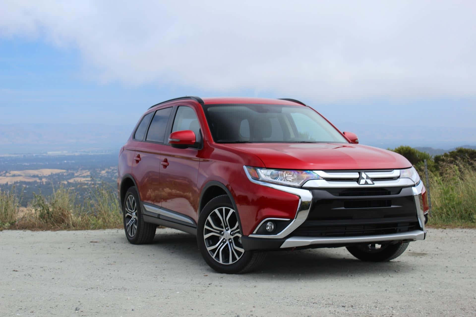 Mitsubishi Asx 桌布 壁紙 — 一輛亮紅色三菱Outlander SUV停泊在碎石觀景點，俯瞰煙霧瀰漫的山谷和遠山，天空多雲。
