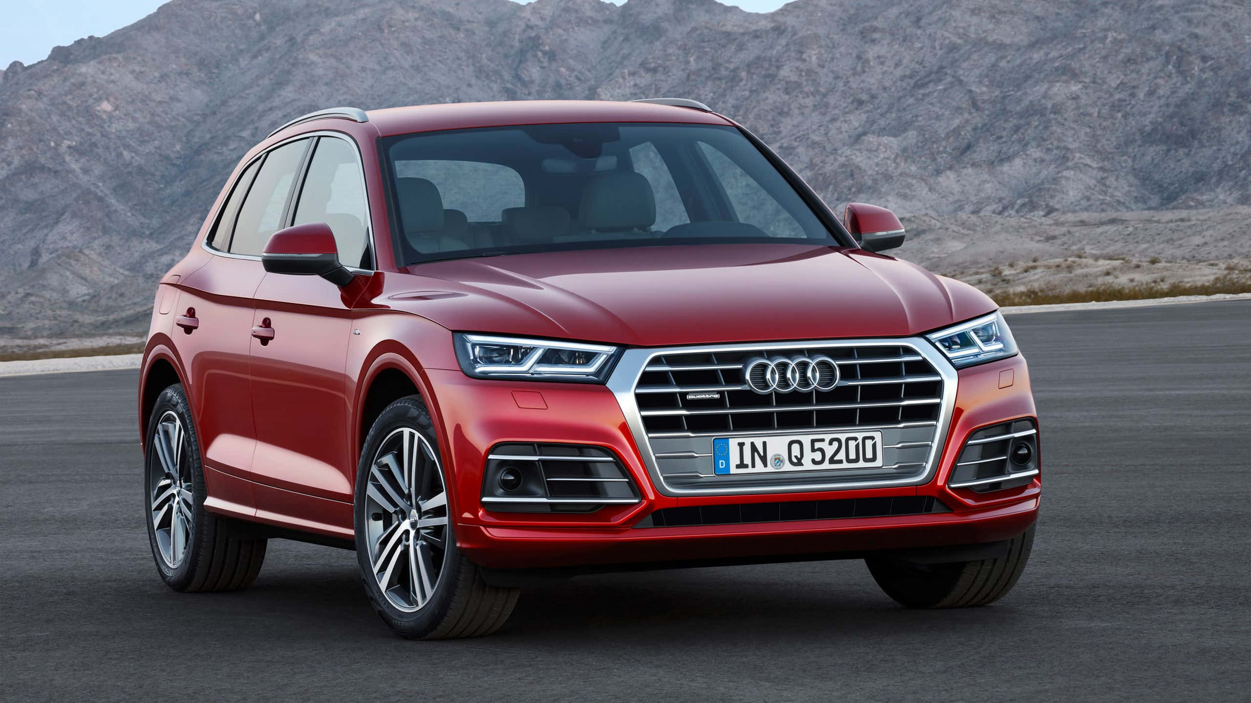 Audi Sq5 桌布 壁紙 — 一輛亮紅色奧迪Q5 SUV停在瀝青路上，背景是岩石山脈，在晴朗的日光下。