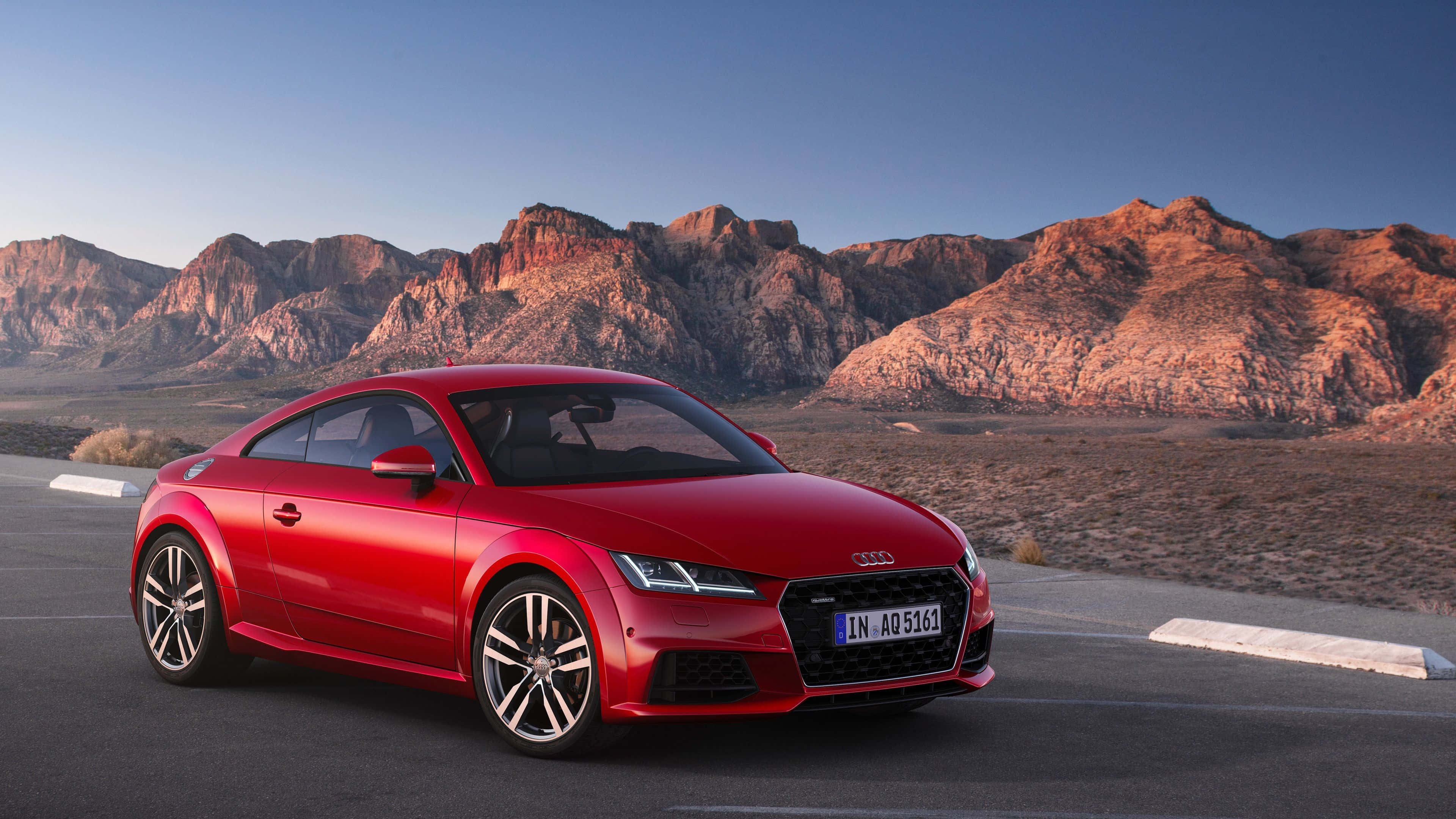 Audi Tt 桌布 壁紙 — 一輛亮紅色奧迪TT轎跑車停在沙漠公路上，背景是崎嶇的山脈，沐浴在金色的夕陽中。