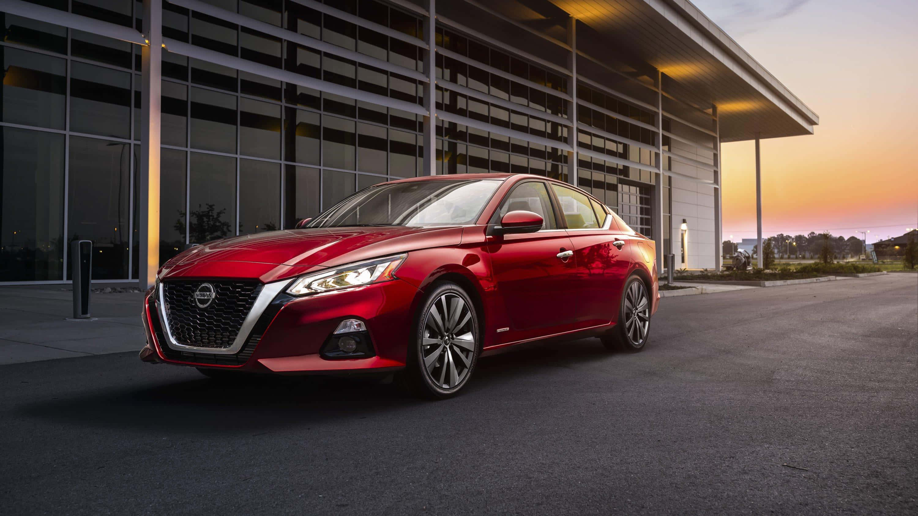 Nissan Altima 桌布 壁紙 — 一輛亮紅色日產Altima房車停放在現代玻璃建築前，正值溫暖的日落時分。