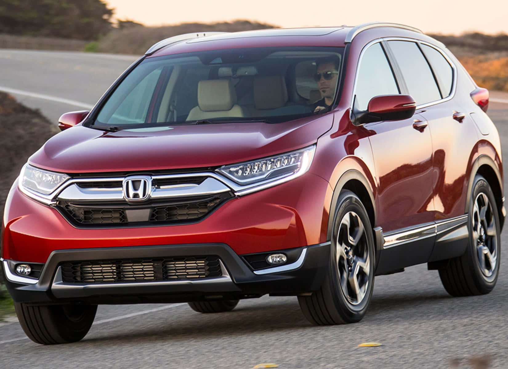 Honda Cr-v 桌布 壁紙 — 一輛亮紅色本田CR-V SUV在日落時分行駛在鋪砌道路上，司機戴著太陽眼鏡。