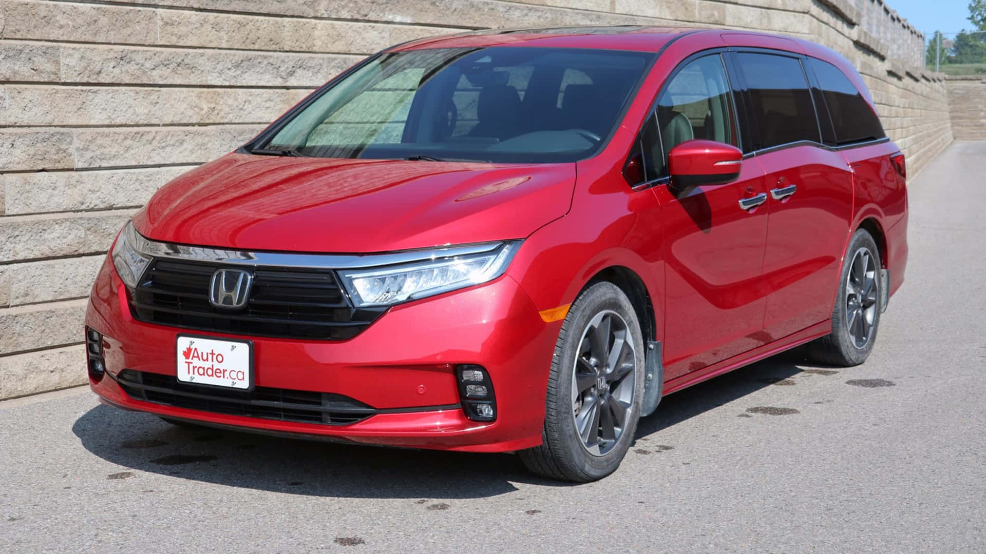 Honda Odyssey 桌布 壁紙 — 一輛亮紅色本田Odyssey廂型車停在柏油路上，旁邊是石牆，在明亮的日光下。