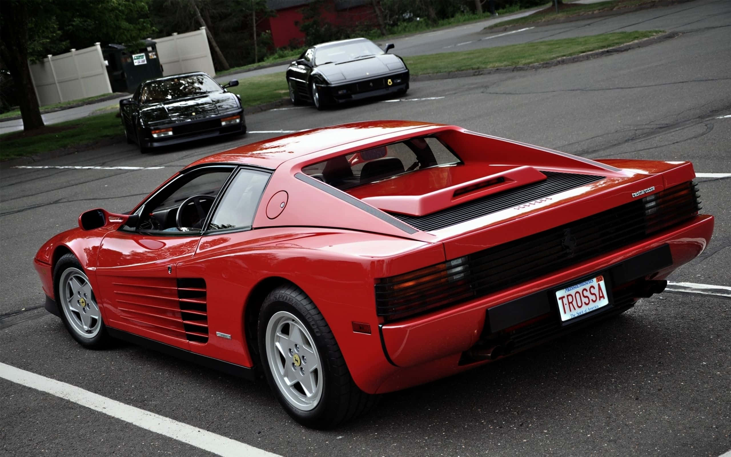 Ferrari Testarossa 桌布 壁紙 — 一輛亮紅色法拉利 Testarossa 停放在停車場，背景有兩輛黑色跑車。