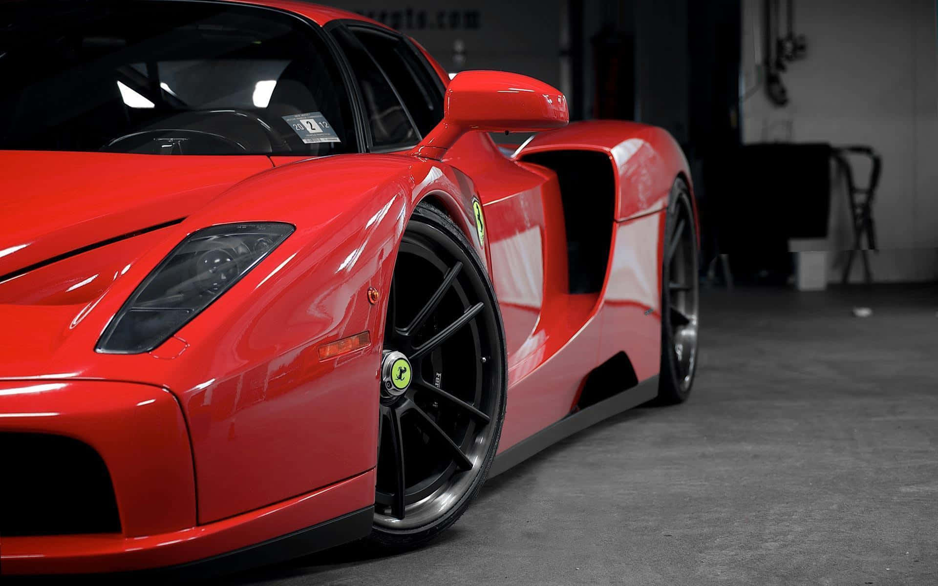 Ferrari Enzo 桌布 壁紙 — 一輛亮紅色法拉利Enzo跑車停放在燈光昏暗的車庫中，配備黑色車輪和綠色中心蓋。