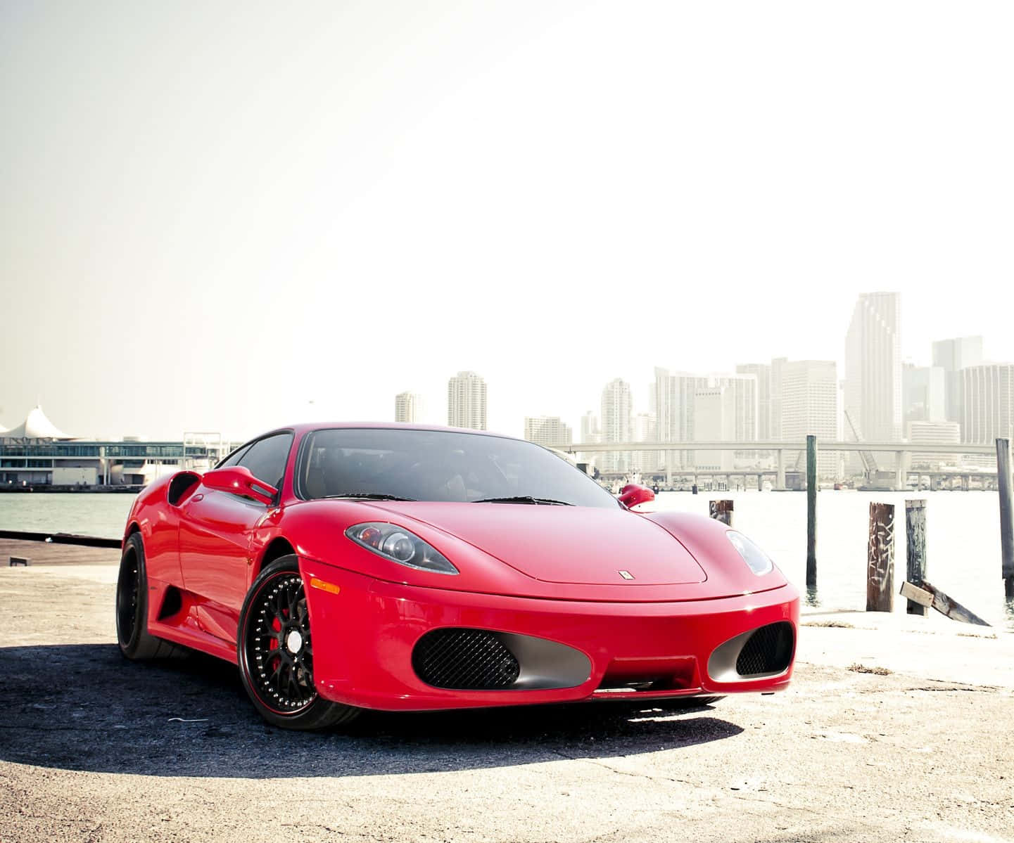 Ferrari 360 Modena 桌布 壁紙 — 一輛亮紅色法拉利F430跑車停泊在海濱碼頭，背景是模糊的城市天際線。