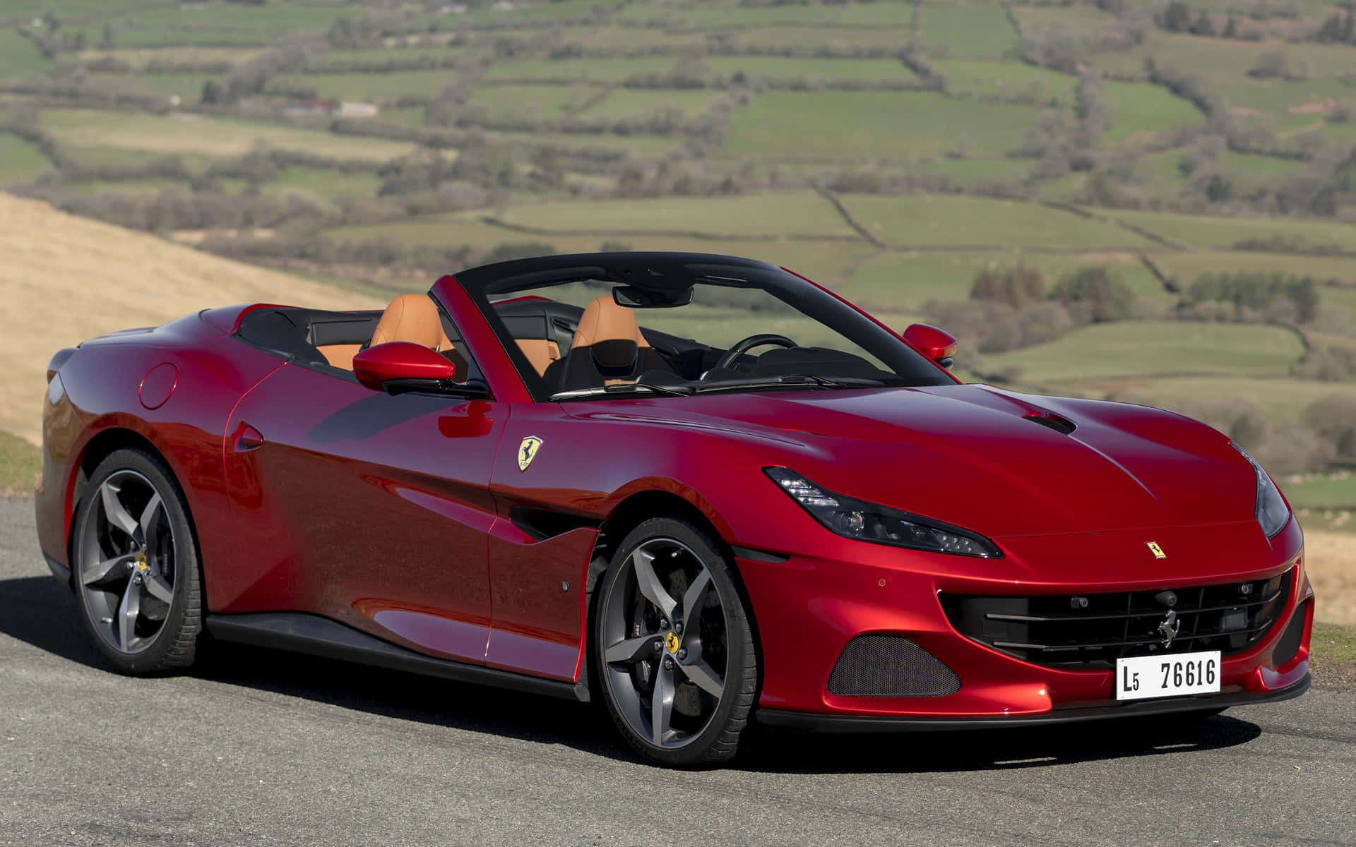 Ferrari Portofino 桌布 壁紙 — 一輛亮紅色法拉利Portofino敞篷車停在一條蜿蜒的道路上，背景是起伏的綠色山丘。