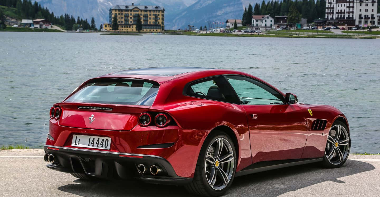 Ferrari Gtc4lusso 桌布 壁紙 — 一輛亮紅色法拉利跑車停泊在寧靜的湖邊，背景有山脈和一座黃色酒店。